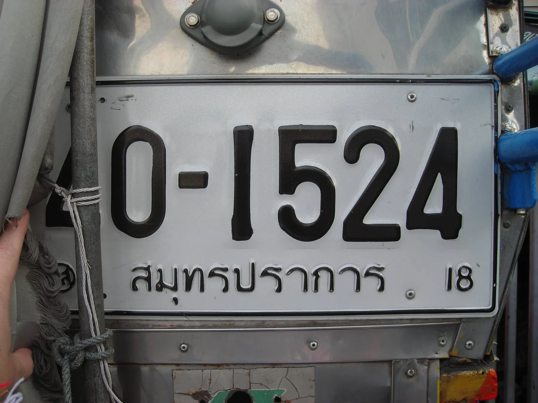 A Thai number plate on the back of a songthaew with part of the registration obscured by a fitting