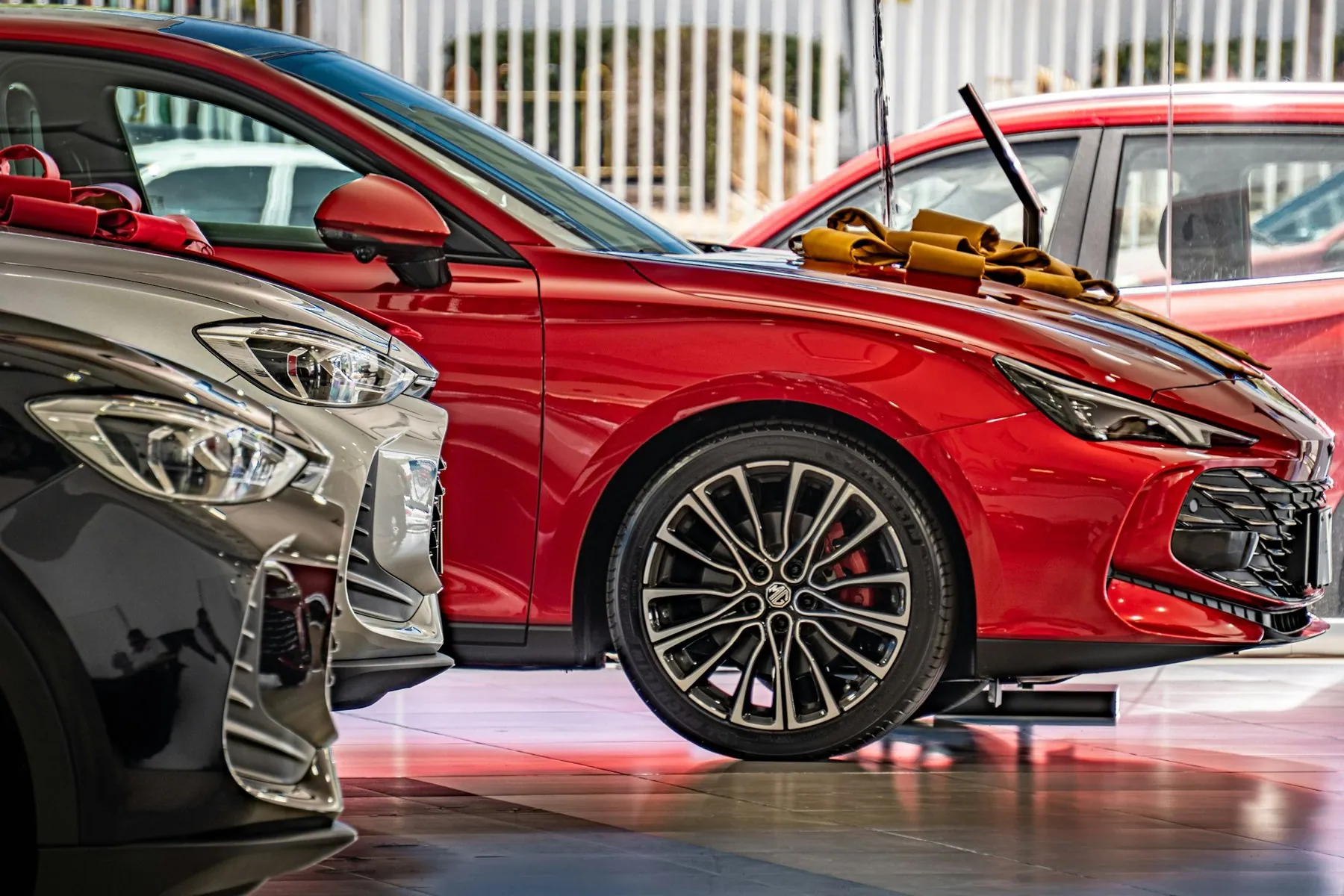 New cars parked in a bright showroom with polished floors, a red hatchback nearest the camera