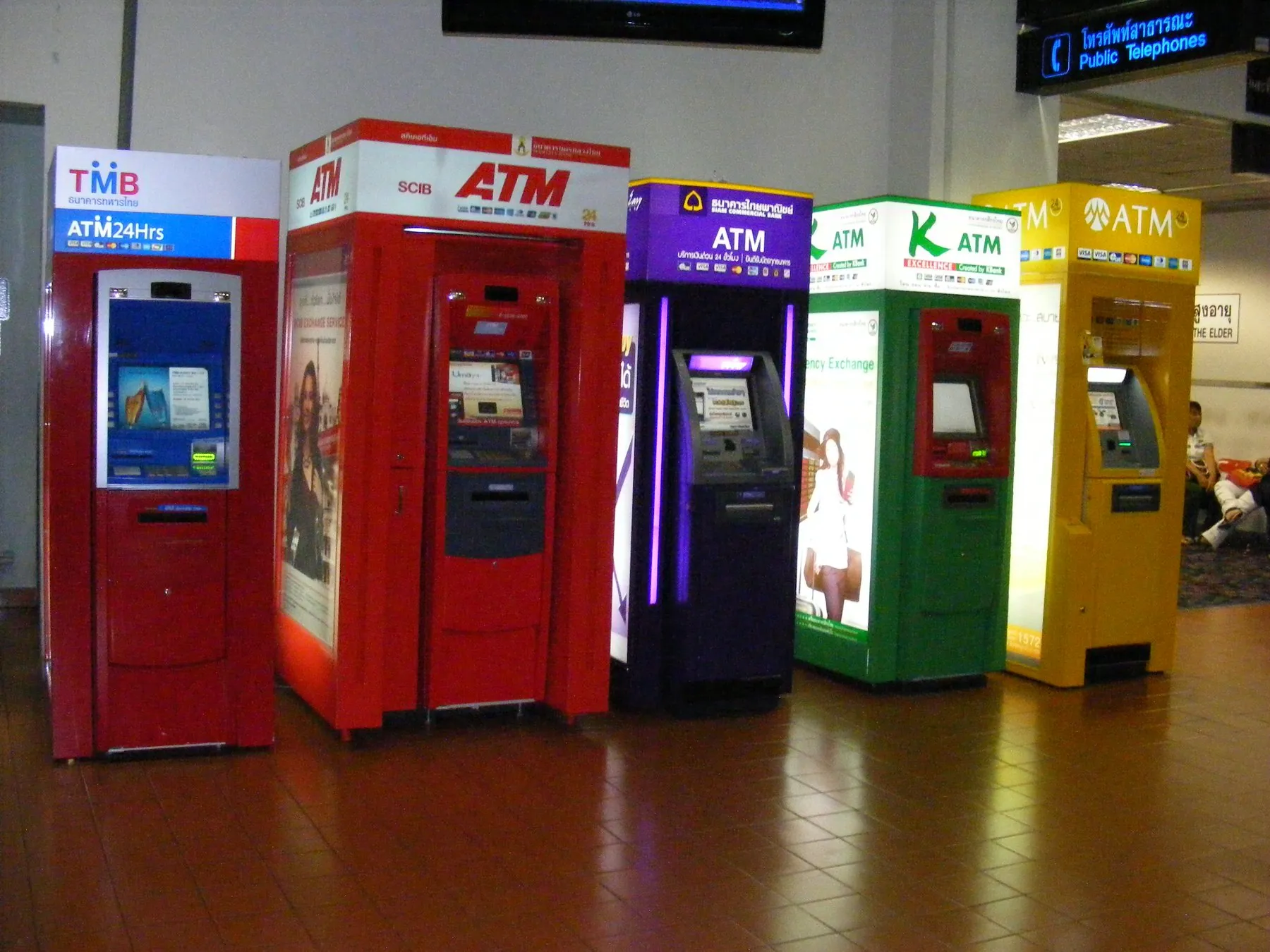 A row of red, purple, green and yellow Thai bank cash machines standing against a wall in the domestic terminal at Don Mueang Airport
