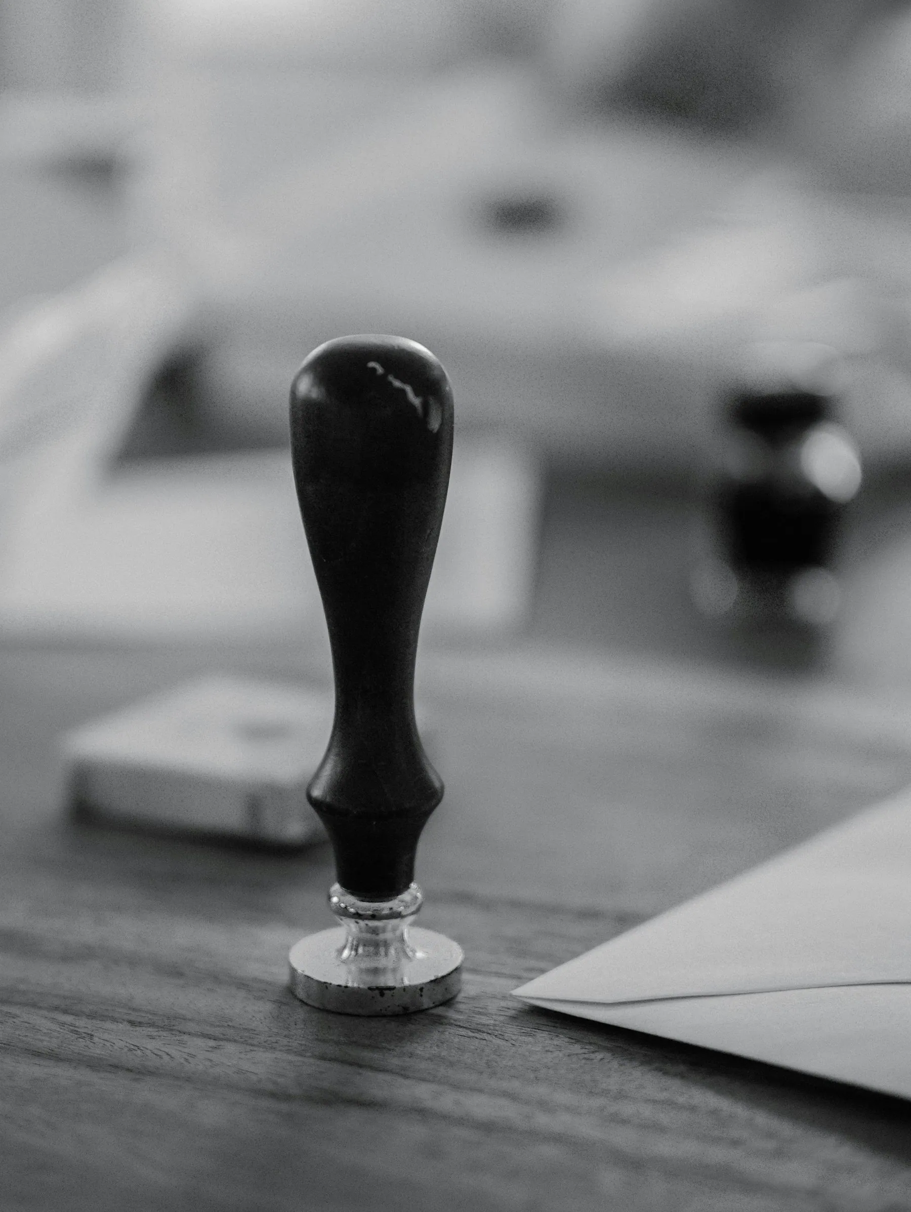 A wooden-handled rubber stamp standing on a desk beside a sheet of paper