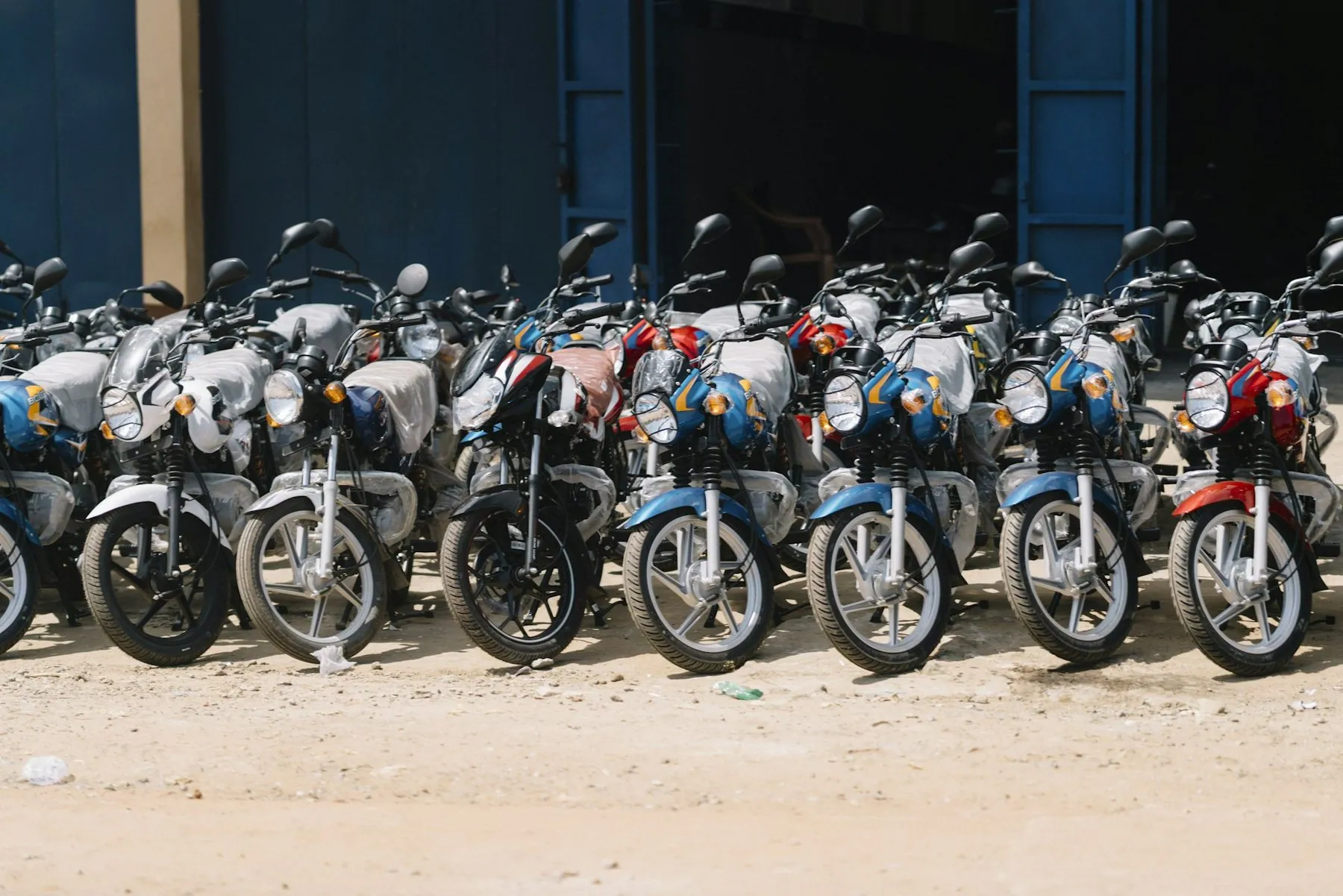 A long row of motorbikes left standing on their side stands on bare ground, none of them moved for some time