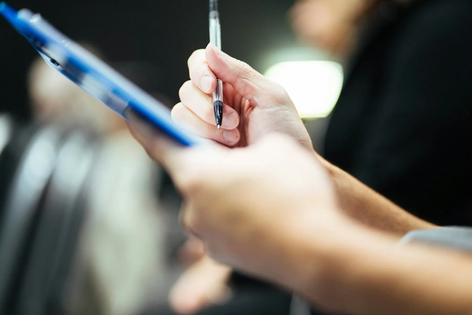 A hand holding a pen poised over a printed agreement clipped to a blue clipboard