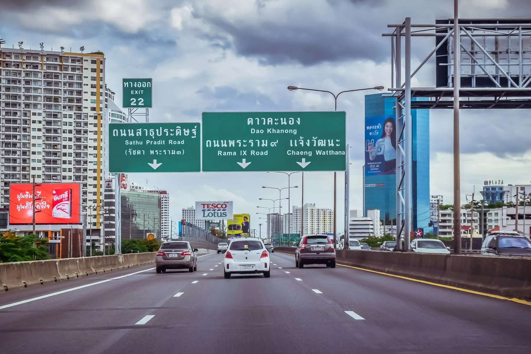 Traffic on a Bangkok elevated highway running away between green Thai direction gantries and city towers