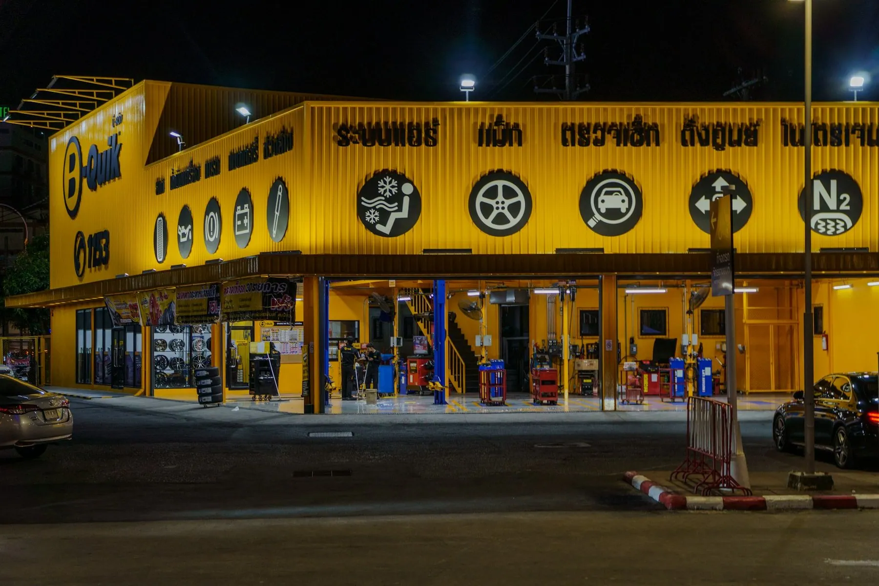 A yellow-fronted tyre and servicing centre in Patong lit up at night, its open bays holding ramps, jacks and stacked tyres