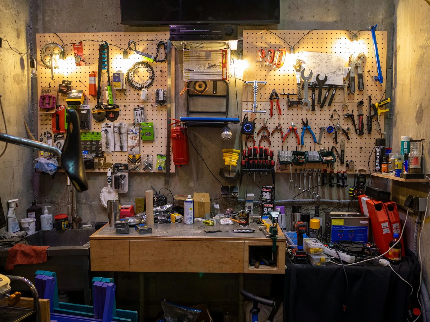 A workshop pegboard hung with spanners and pliers above a workbench of parts and oil cans