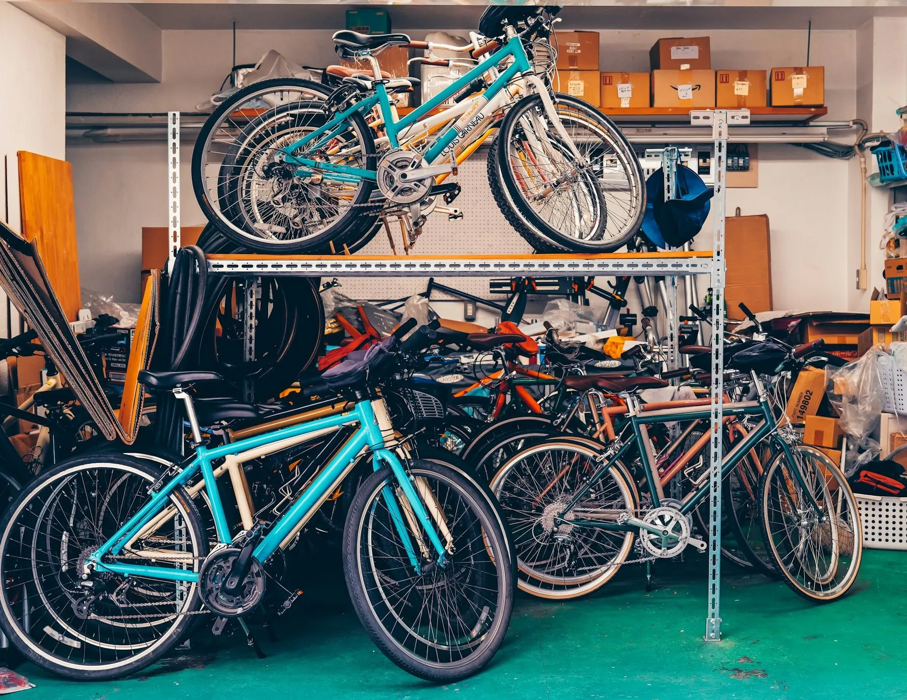 Bicycles packed onto steel shelving and stacked on the floor of a cluttered repair workshop