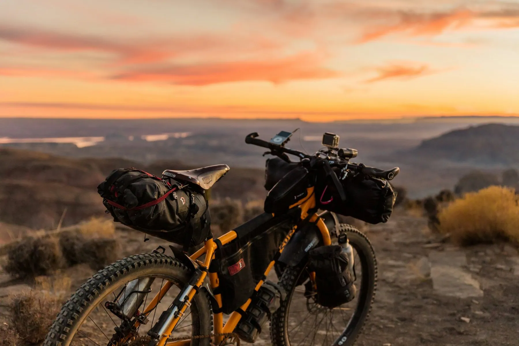A loaded touring bicycle propped up on a grassy ridge with hills receding into haze at sunset