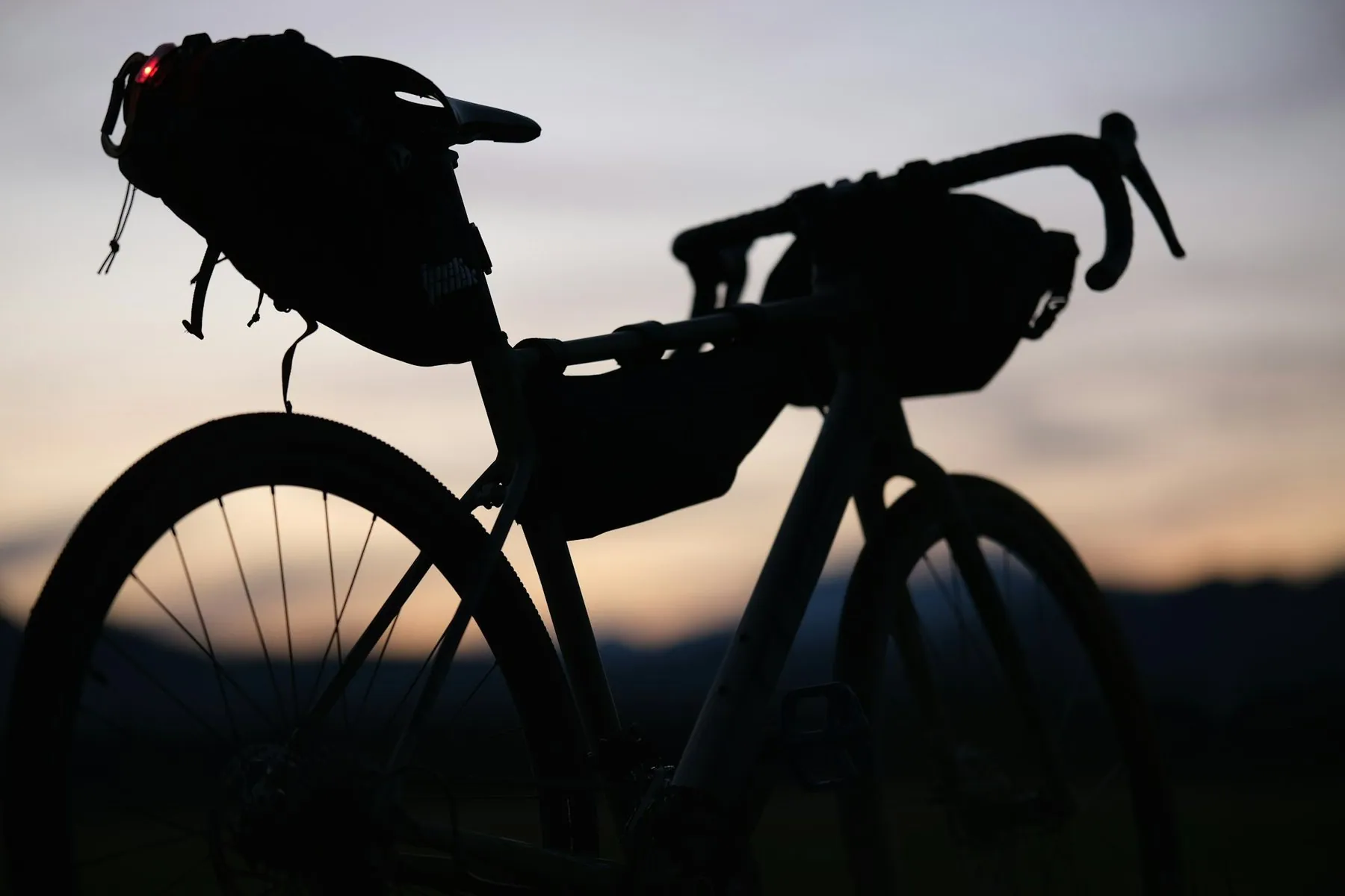 The silhouette of a loaded touring bicycle with handlebar and saddle bags against a pale dusk sky