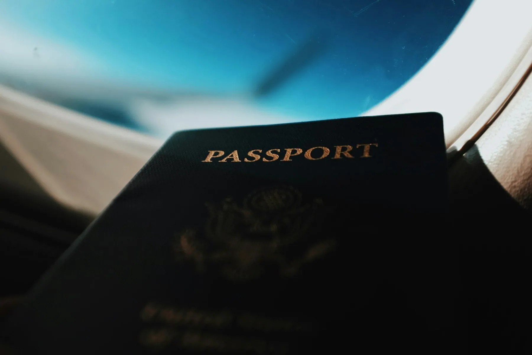 A passport held up against an aircraft window with the wing and sky behind it