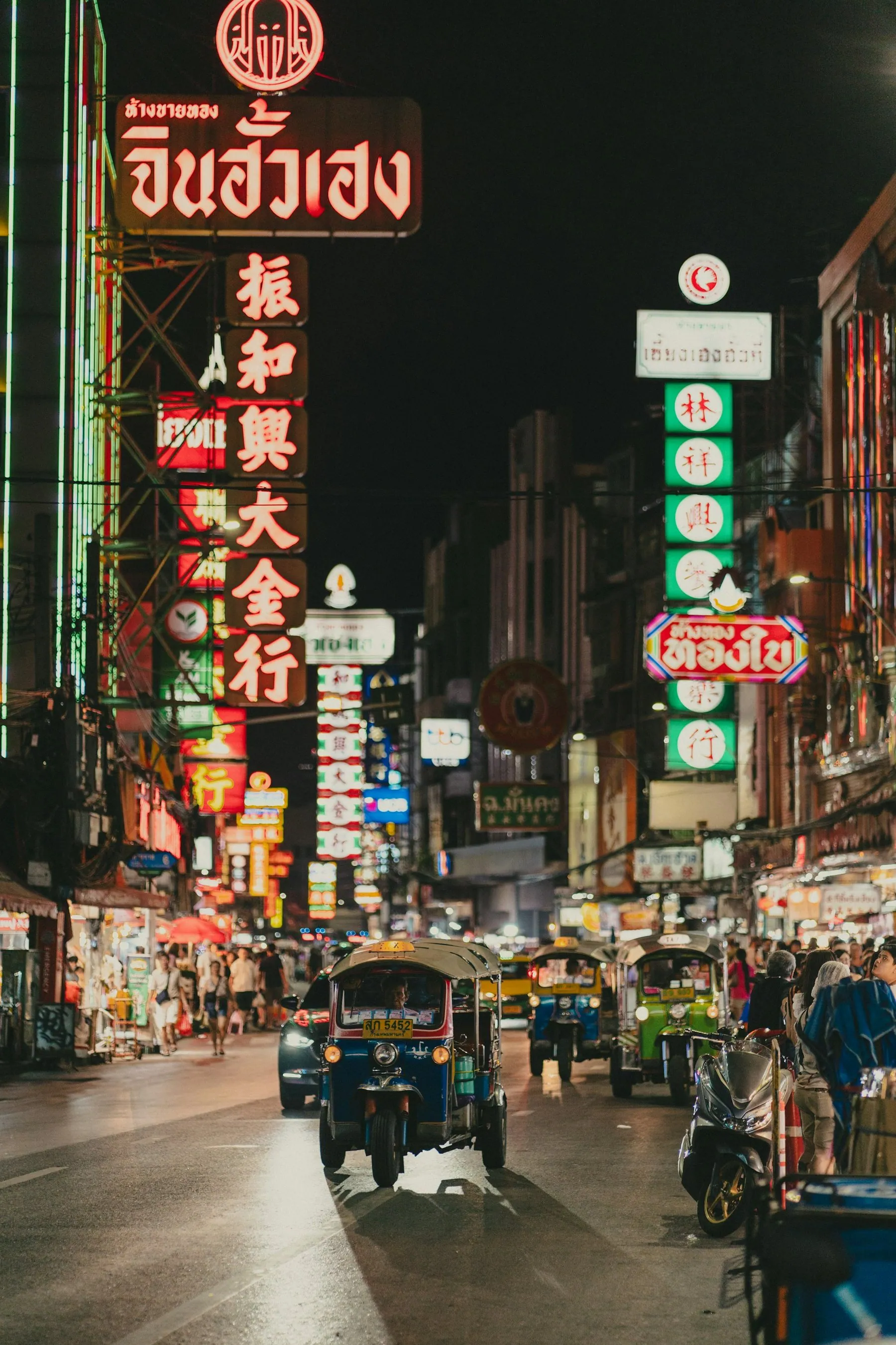 Neon shop signs in Chinese and Thai script above a busy Bangkok street after dark