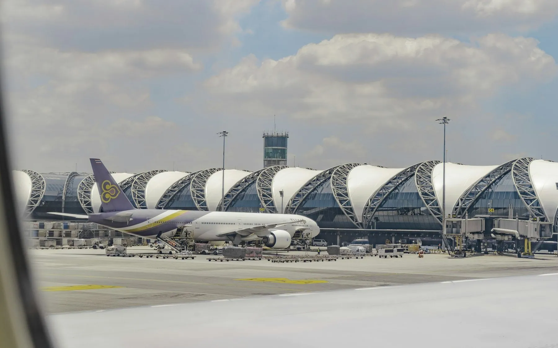 Aircraft parked on the apron in front of the wave-roofed terminal at Bangkok Suvarnabhumi, seen from a cabin window
