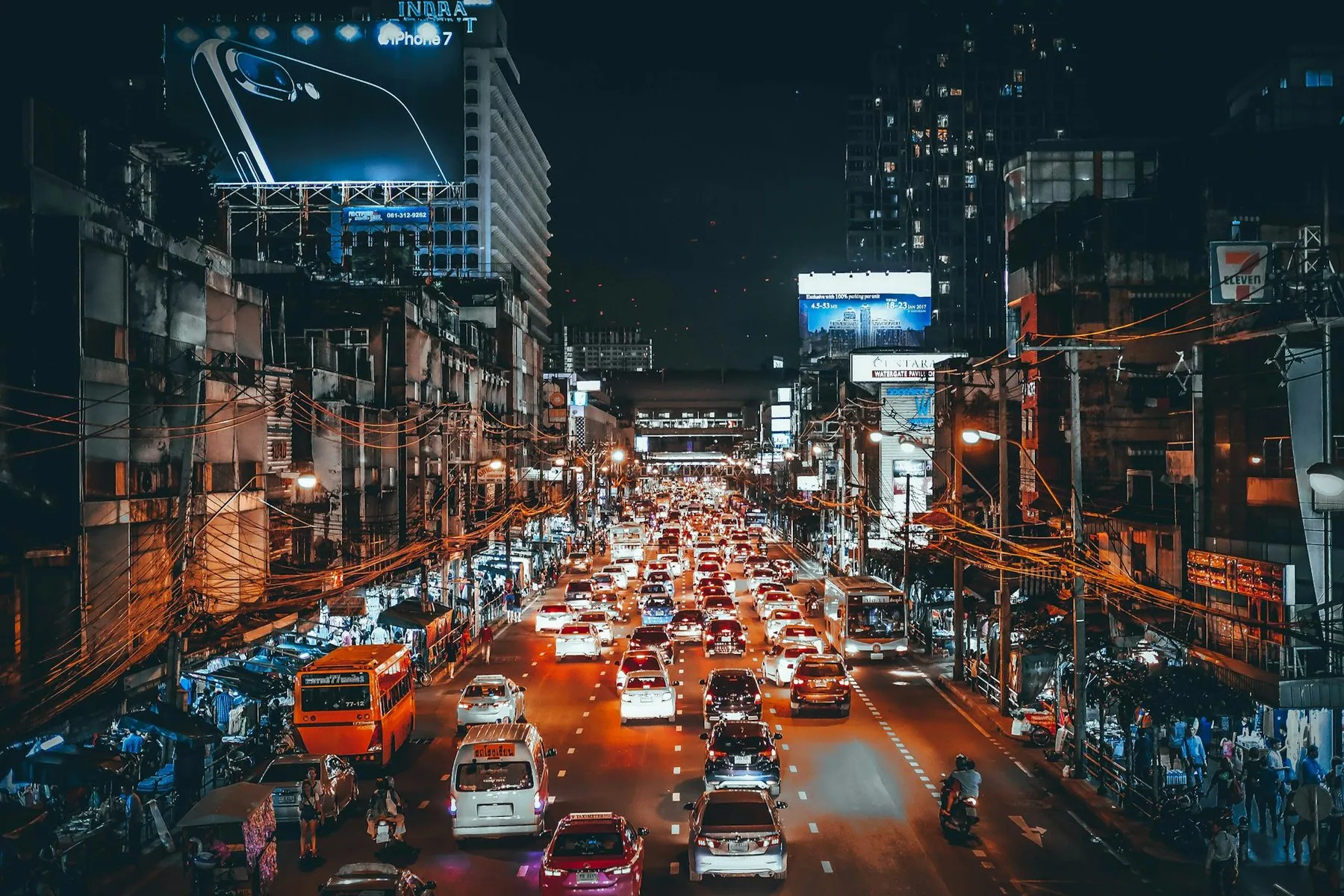 Night traffic running beneath an elevated expressway, headlights and neon reflected on the road