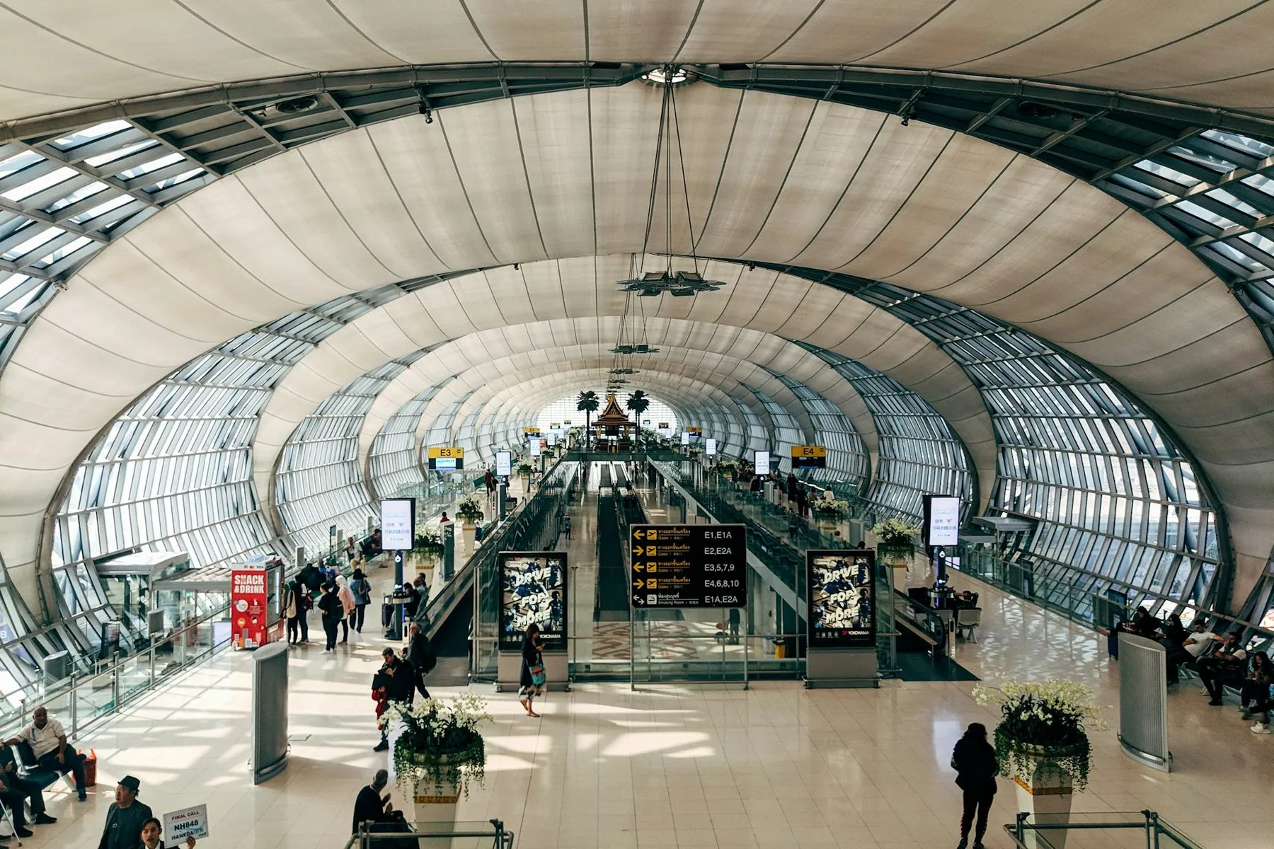 Travellers crossing the wide concourse of Bangkok's Suvarnabhumi terminal under its glass roof arches