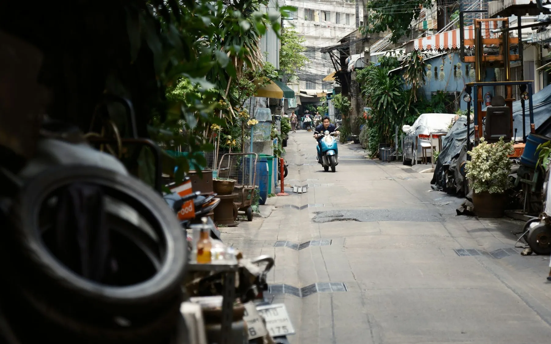 A rider on a small motorbike heading down a narrow residential soi between parked cars