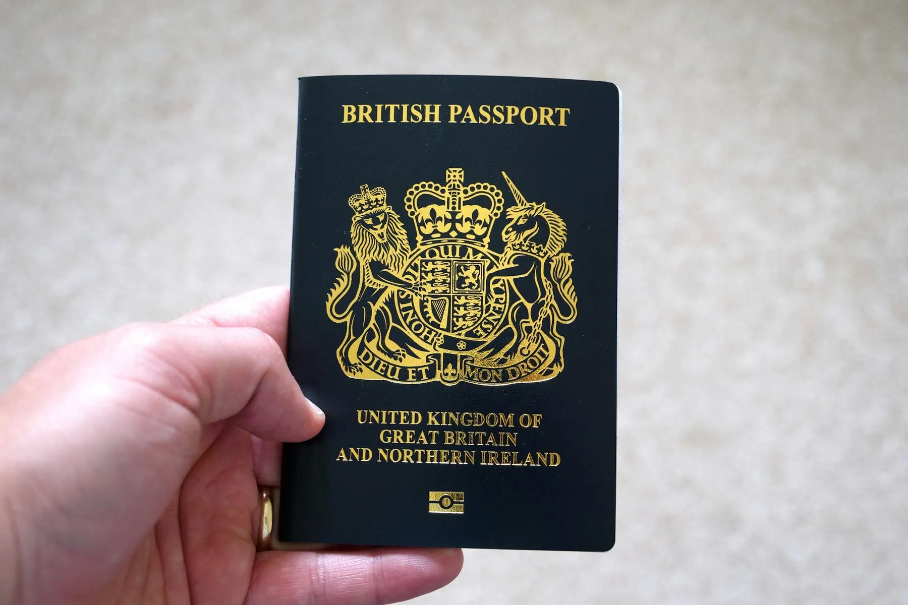 A hand holding a dark blue British passport with the gold crest facing the camera