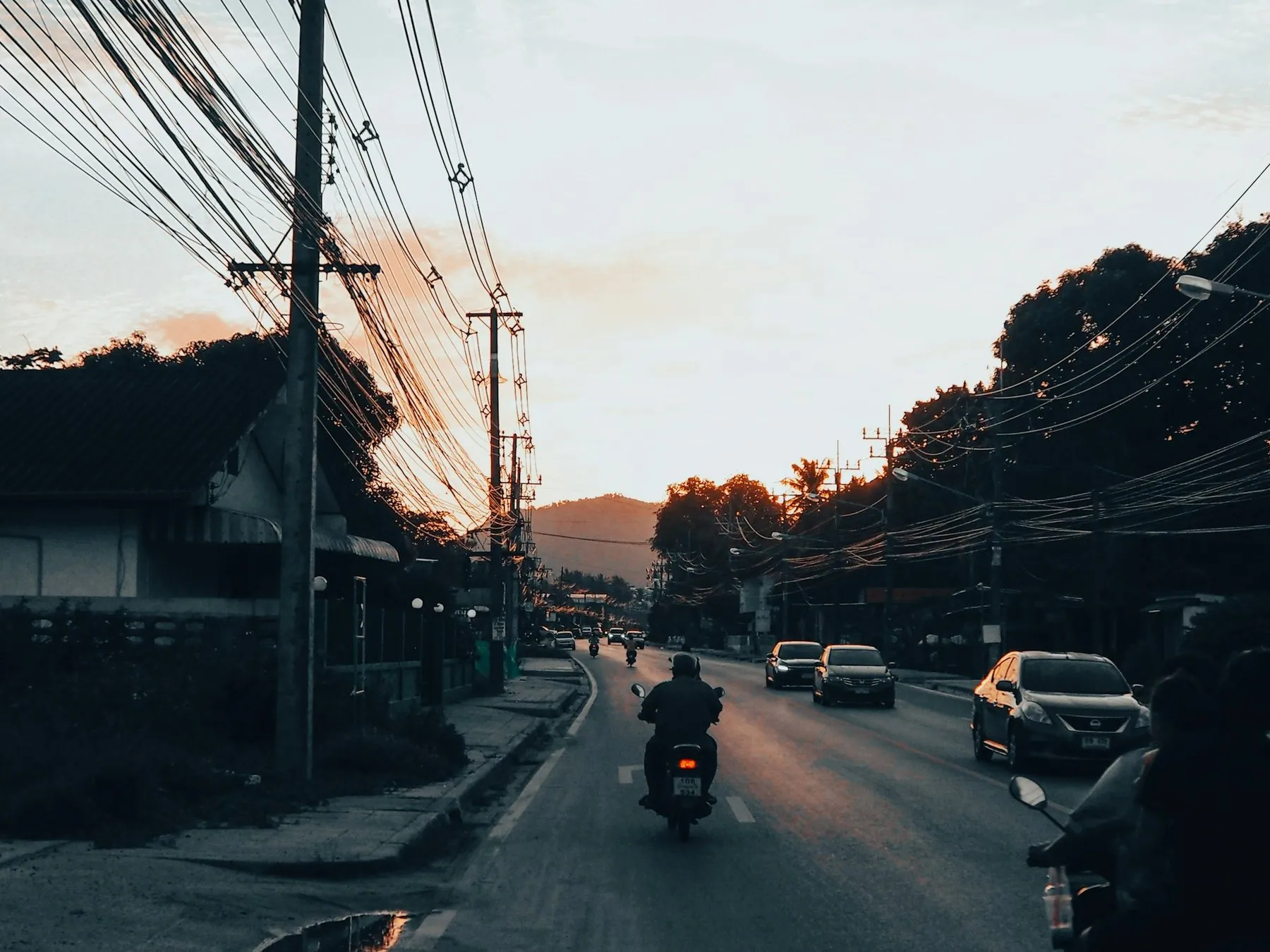 A lone rider heading down a Thai town street at golden hour beneath a tangle of power lines