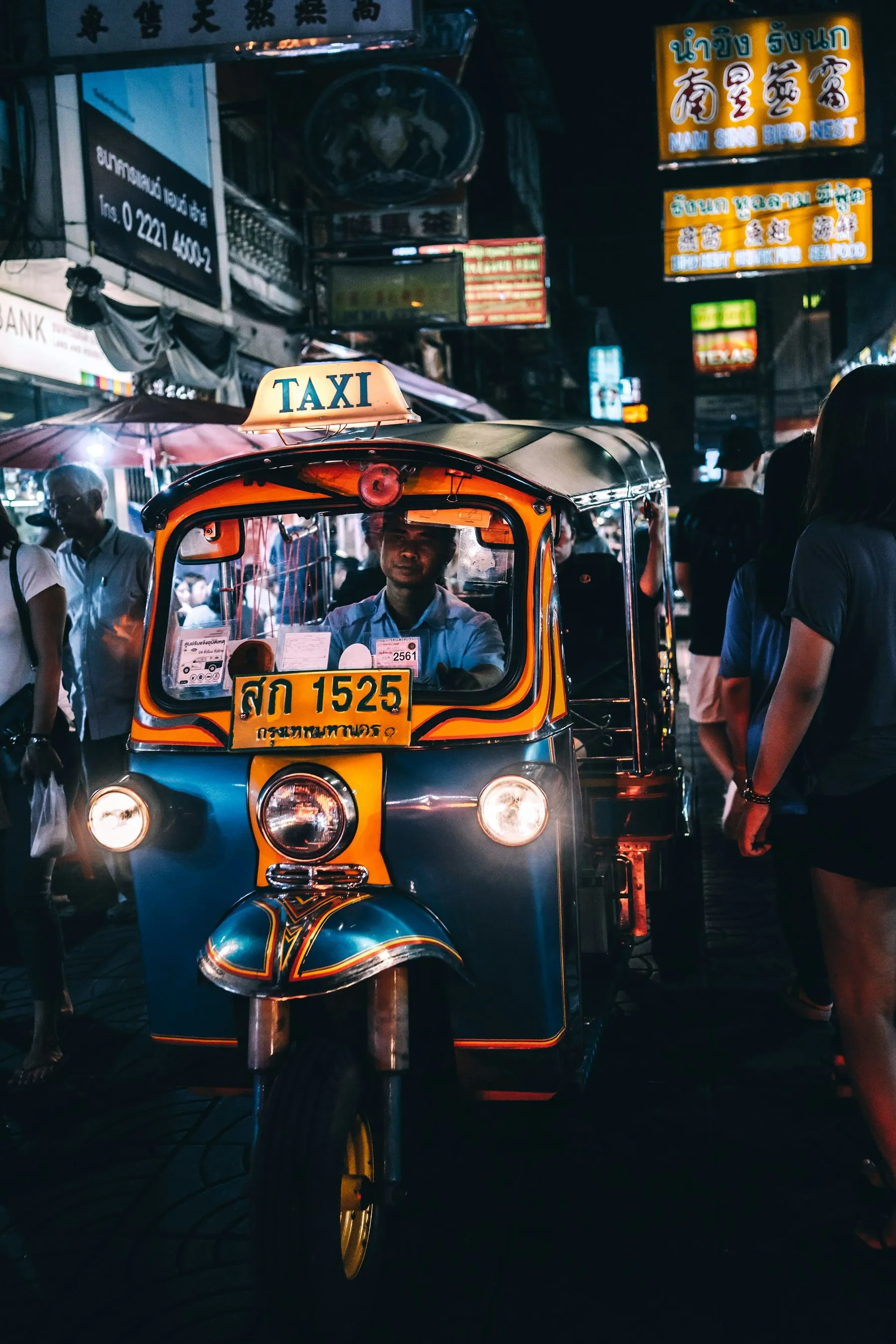 A tuk-tuk with its headlights on waiting under neon signs on a Bangkok street at night