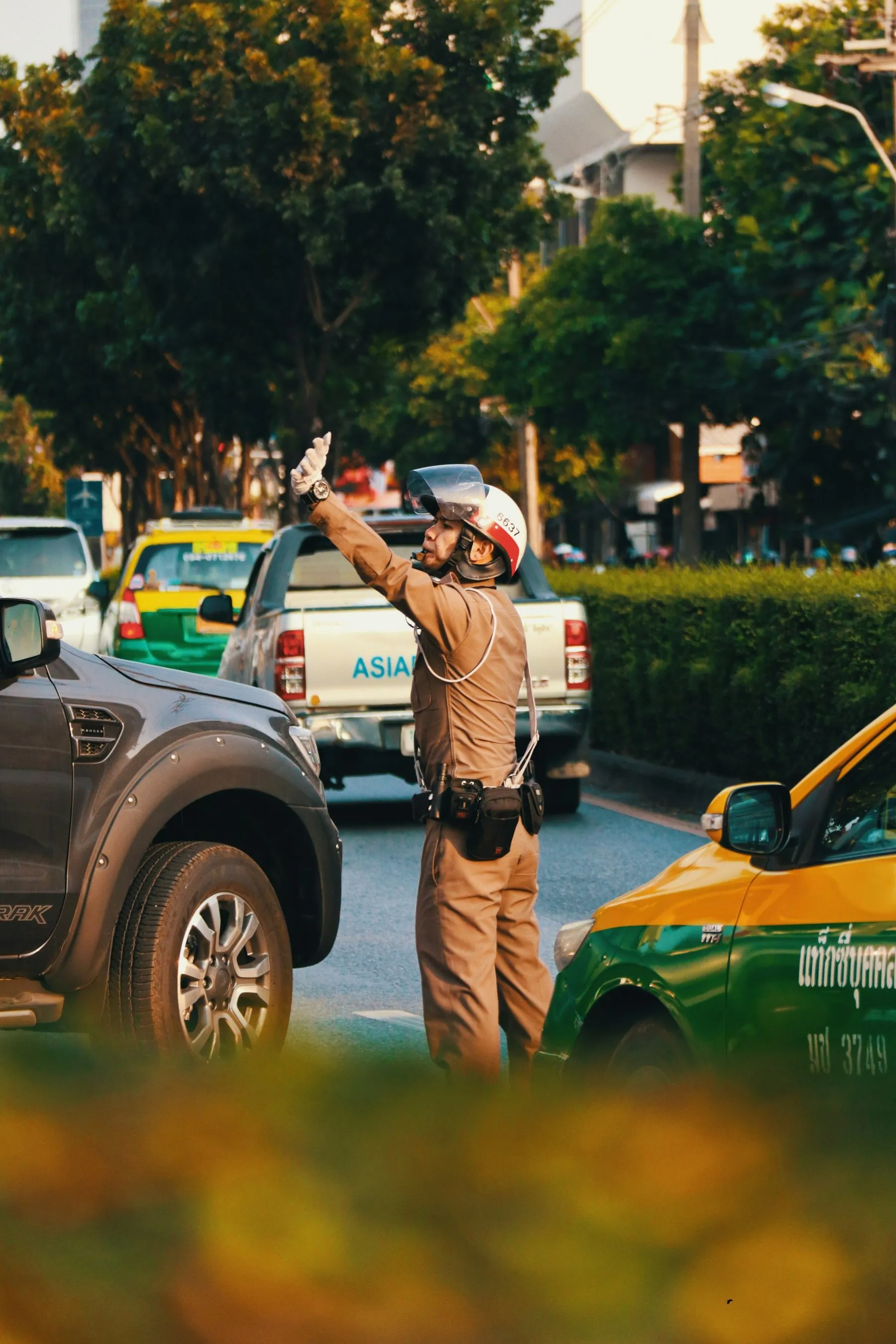 A traffic officer in brown uniform standing in the road directing cars past a green taxi
