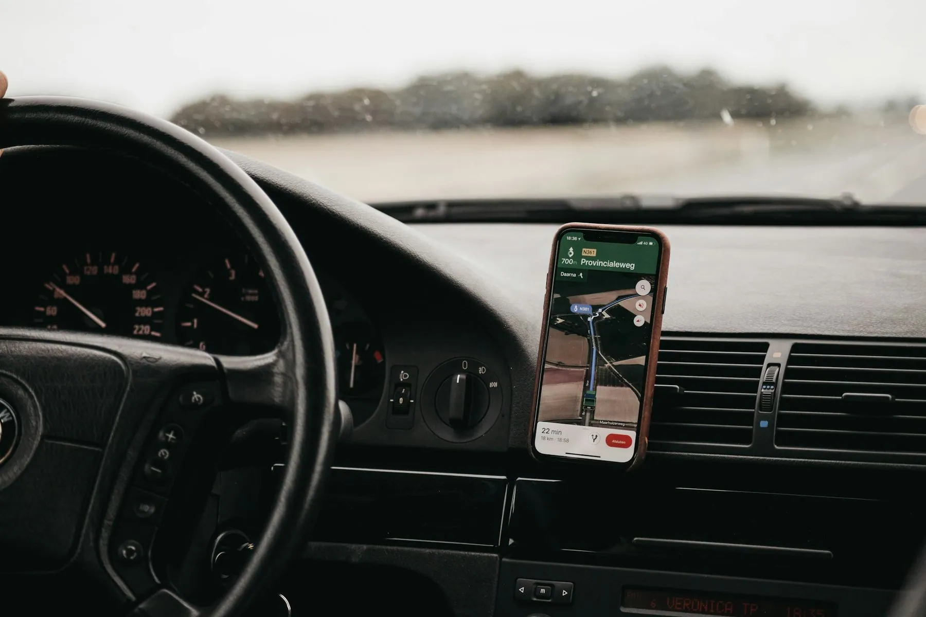 A phone in a dashboard mount showing a map, with the windscreen and road beyond