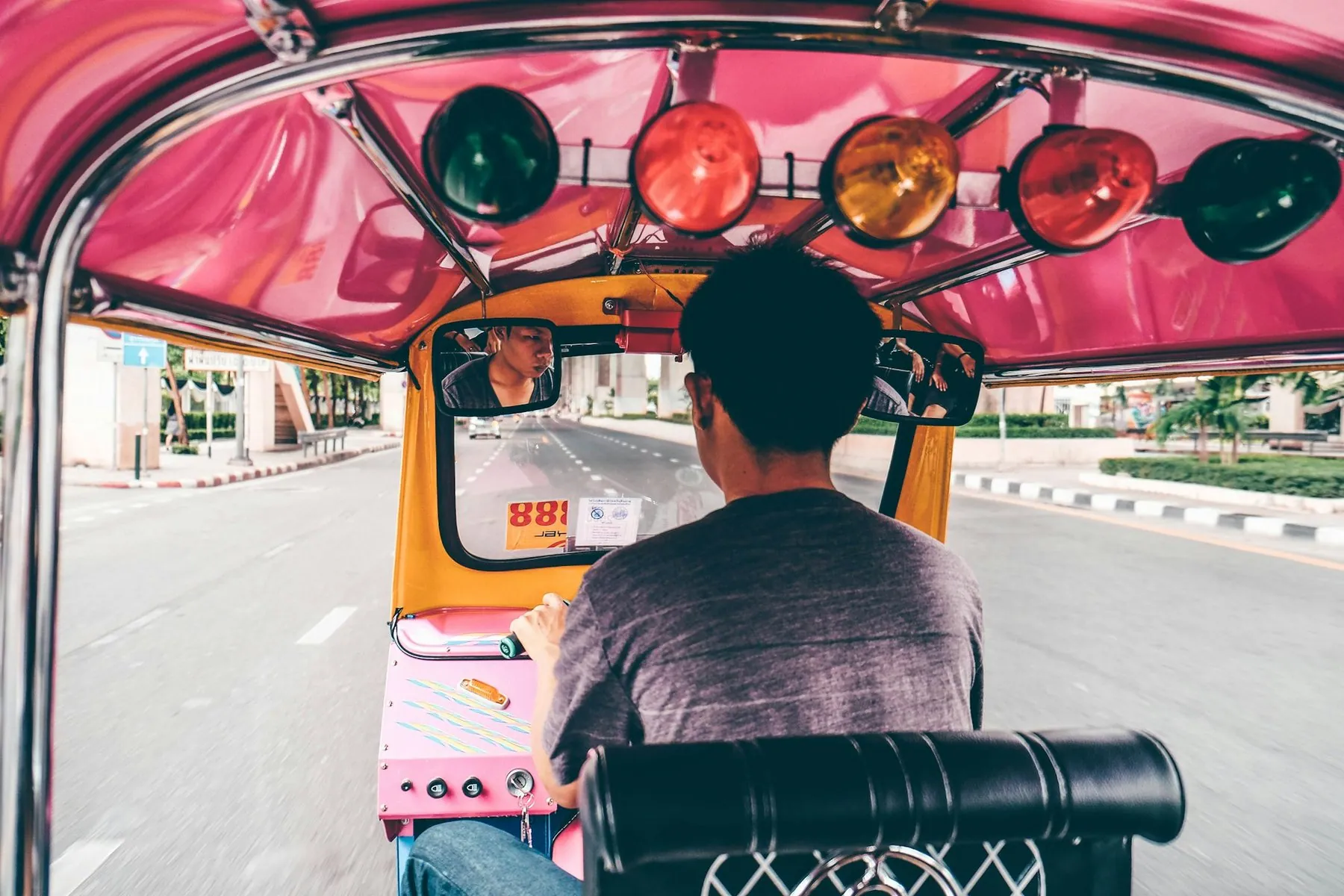 The view from a passenger seat inside a tuk-tuk, over the driver's shoulder and out to the road ahead