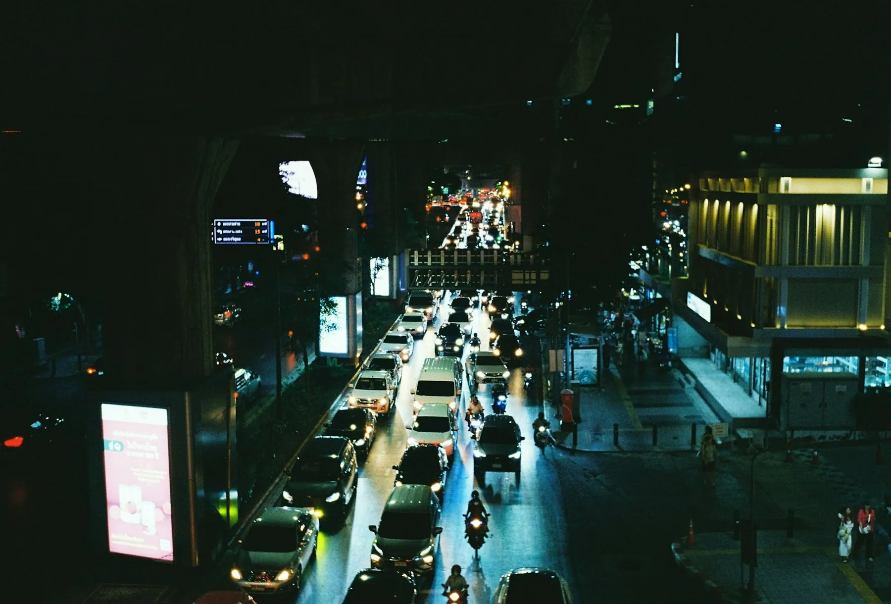 Queued traffic crawling along a wet city street at night, brake lights reflected on the tarmac