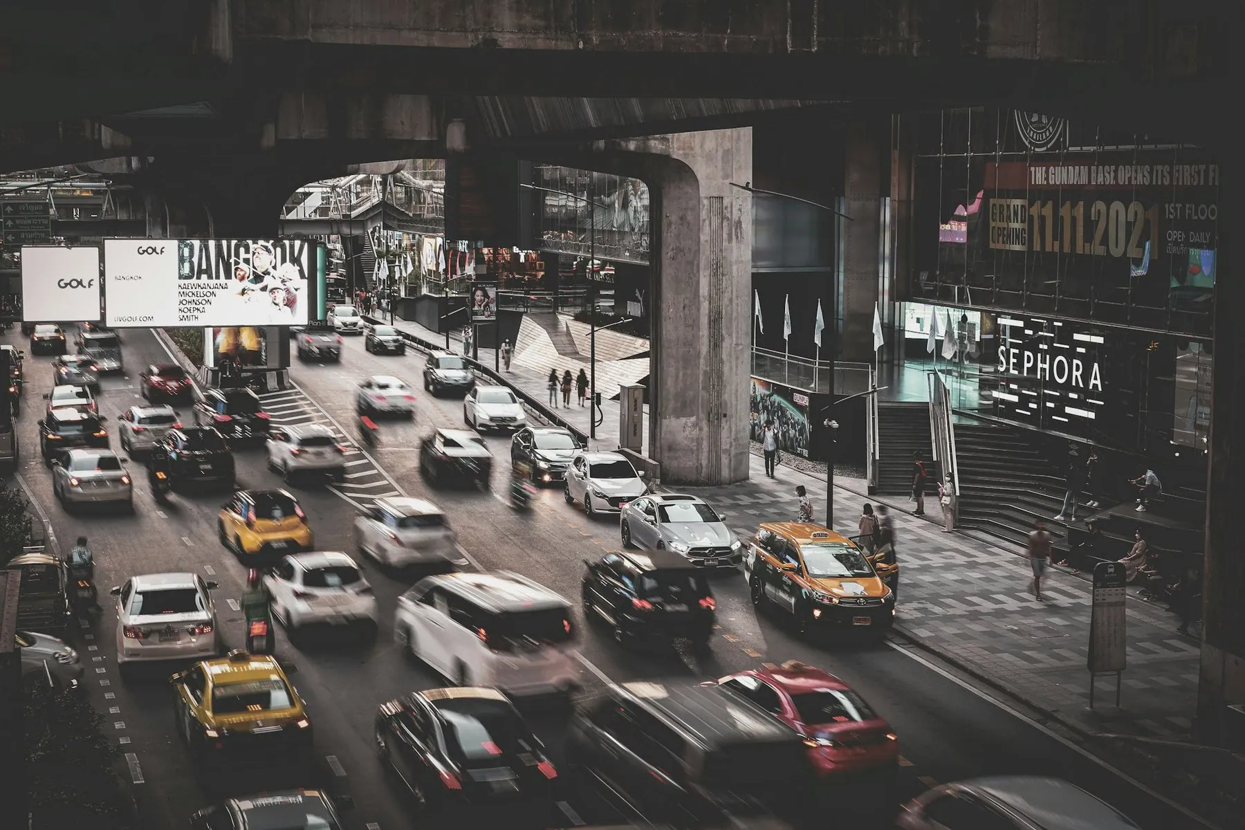 Taxis and cars filling every lane of a Bangkok avenue beneath the concrete deck of the Skytrain