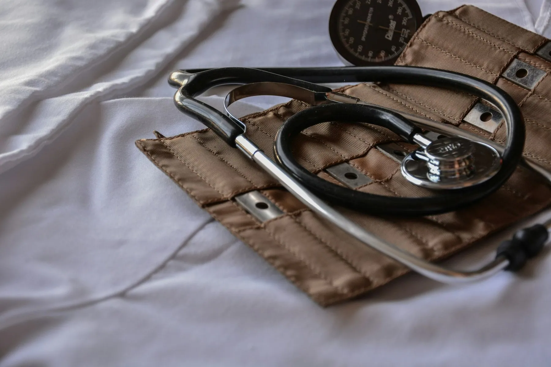 A stethoscope resting on a folded blood-pressure cuff on a white sheet