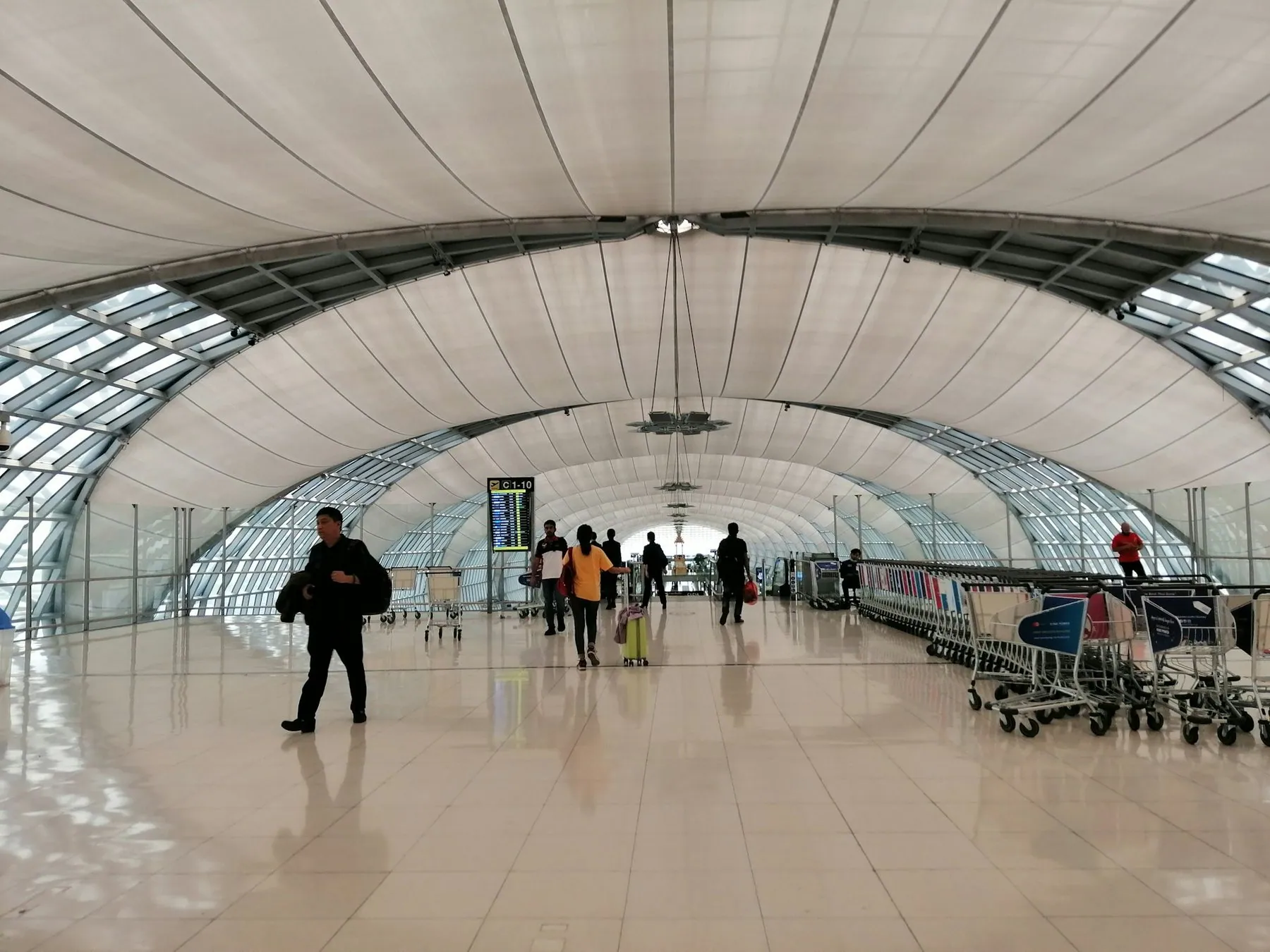 Passengers and luggage trolleys in the long white departures concourse of Bangkok Suvarnabhumi