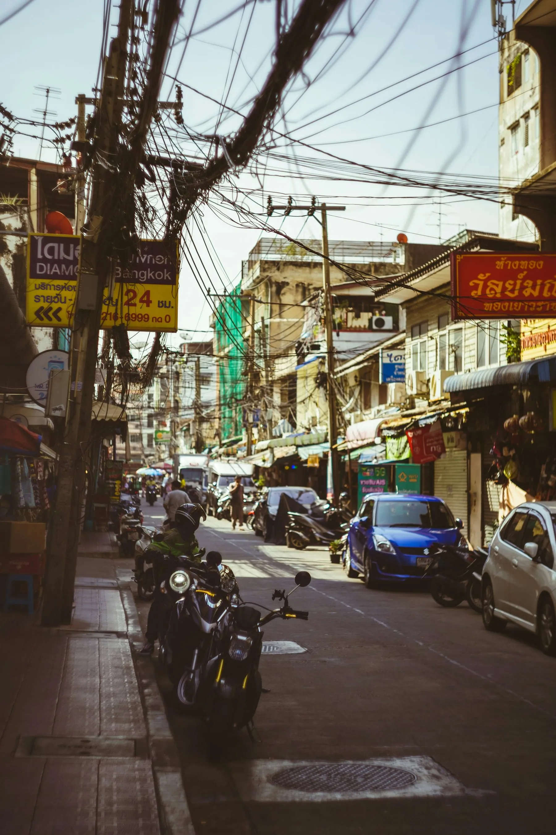 Motorbikes and cars sharing a narrow Thai shopping street lined with signboards
