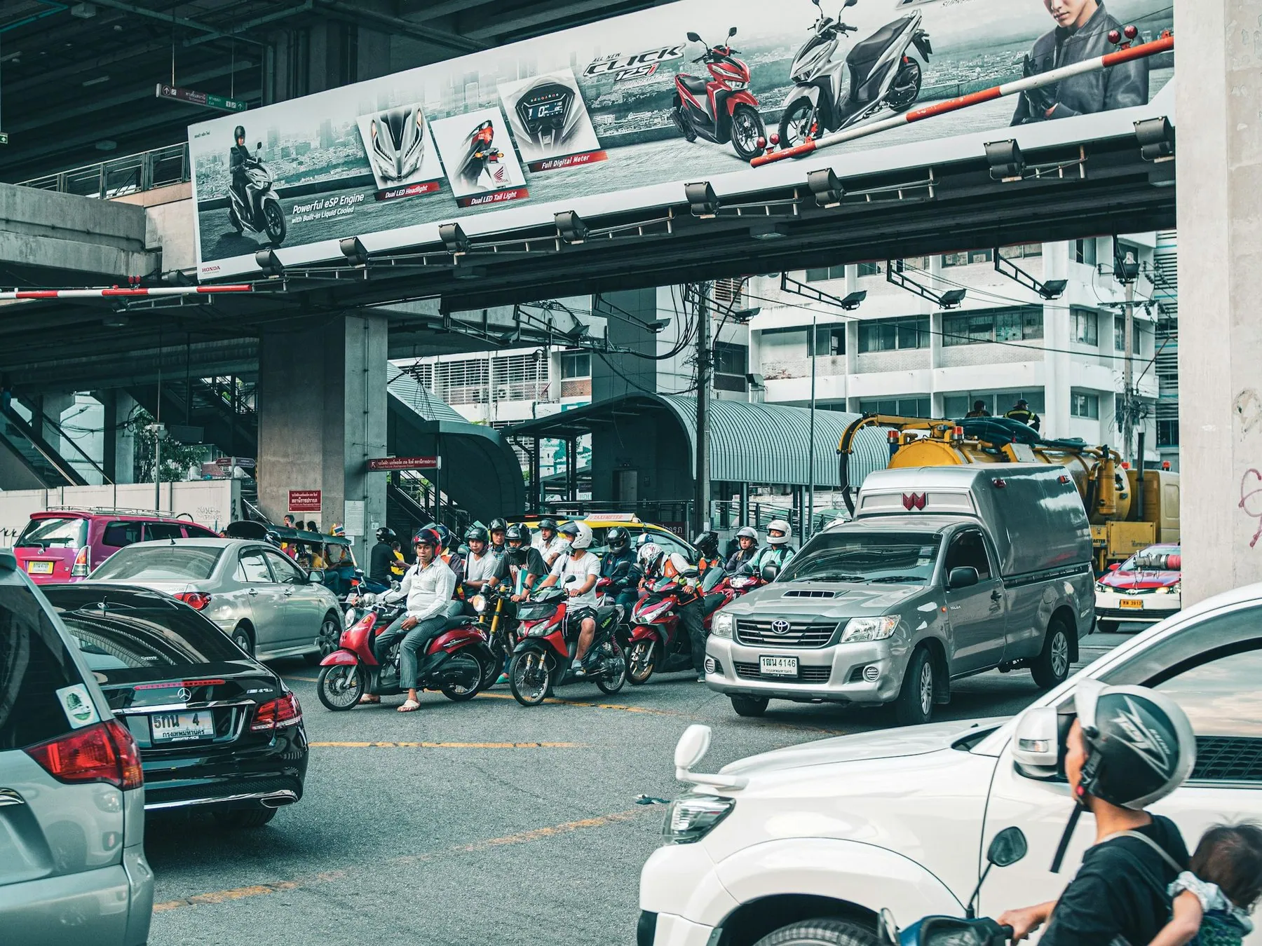 A pack of riders waiting on their motorbikes at a red light in Bangkok, pickups and cars alongside them