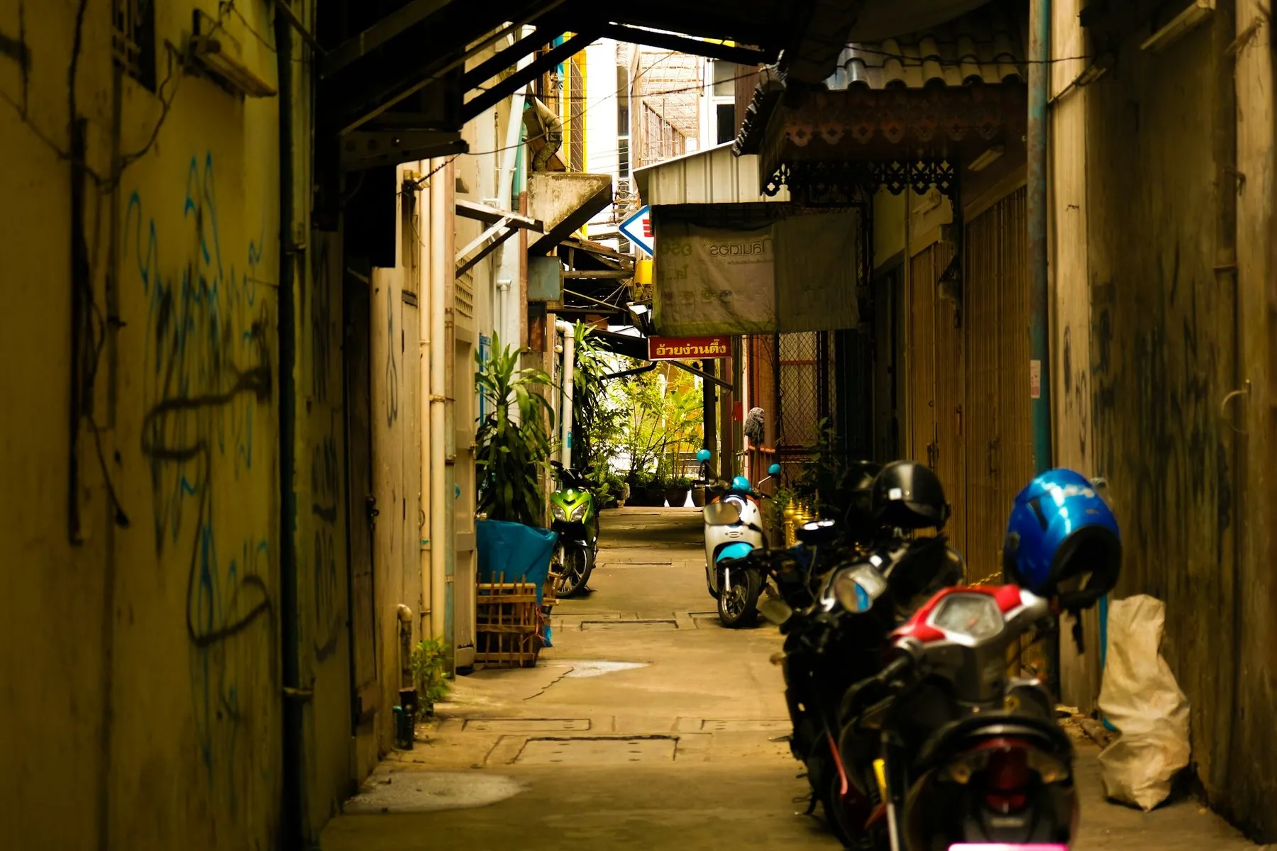 Motorbikes parked in a line down a narrow alley between weathered shophouse walls