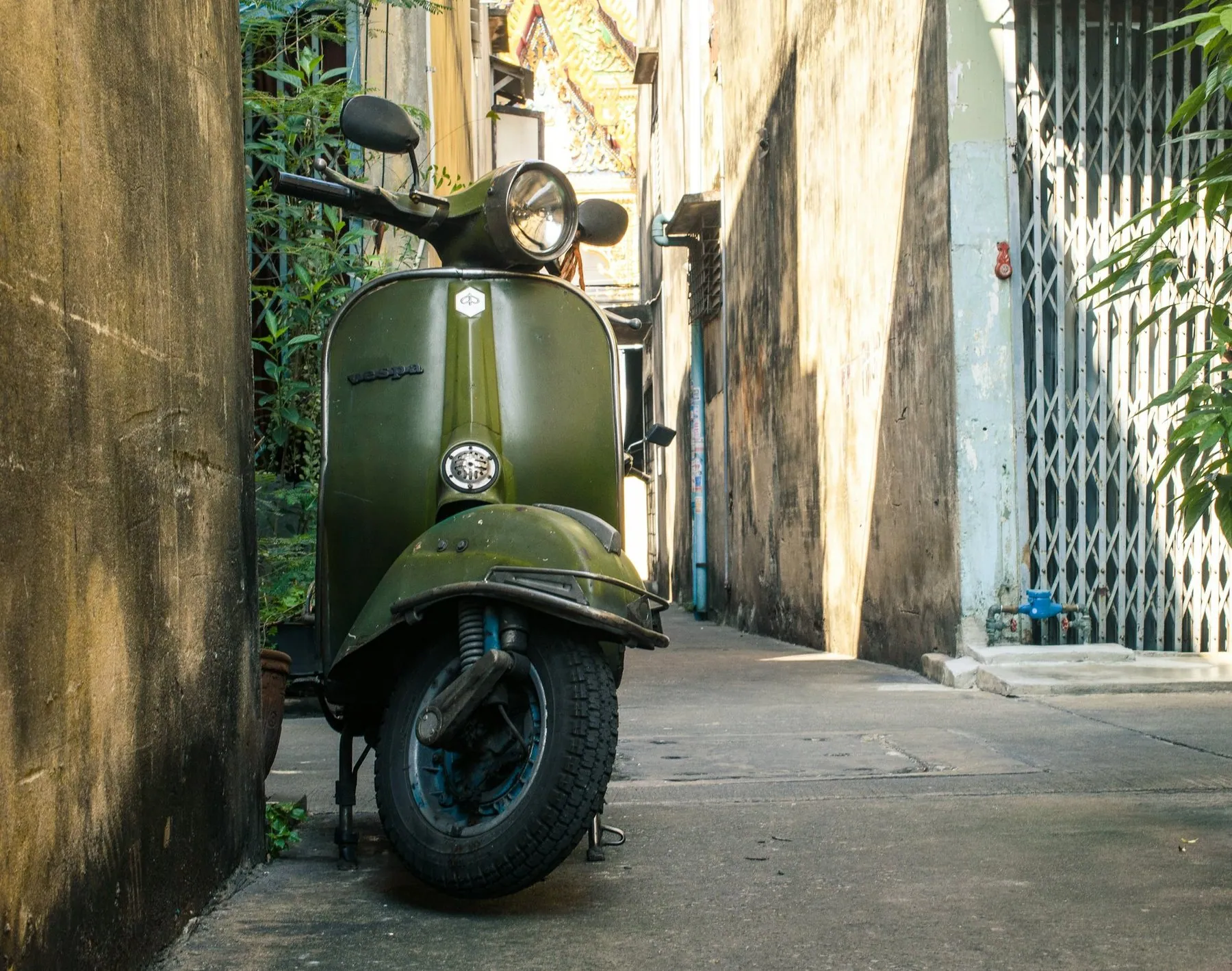 A small dark green scooter parked against a wall in a narrow alley