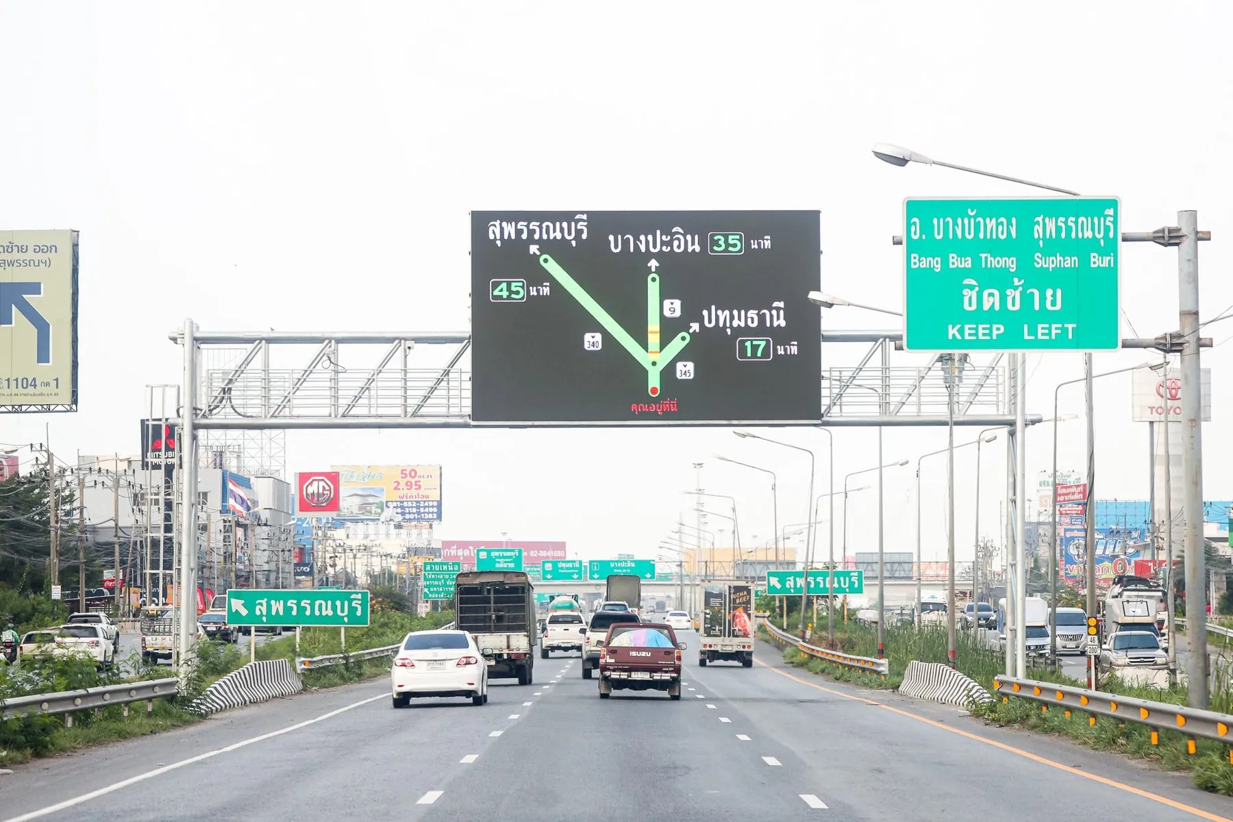 An overhead gantry across a Thai motorway carrying a matrix sign and lane arrows in Thai script
