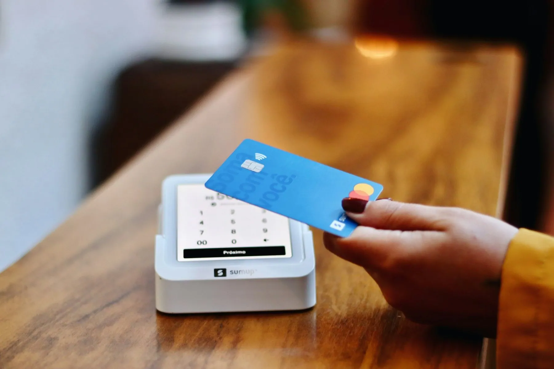 A blue bank card being pushed into the slot of a small white card reader standing on a wooden counter