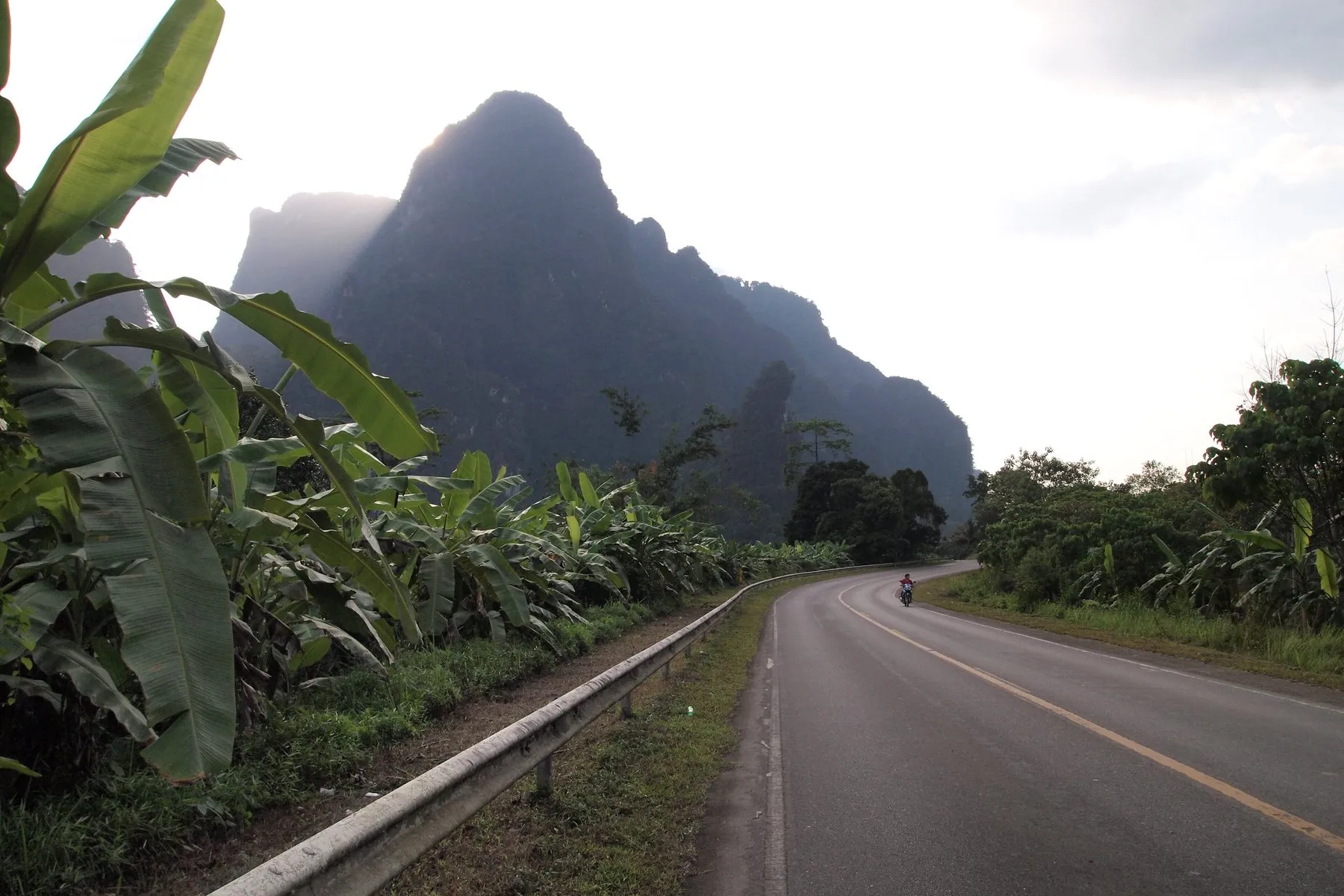 An almost empty highway curving through jungle in Surat Thani province with a limestone peak ahead