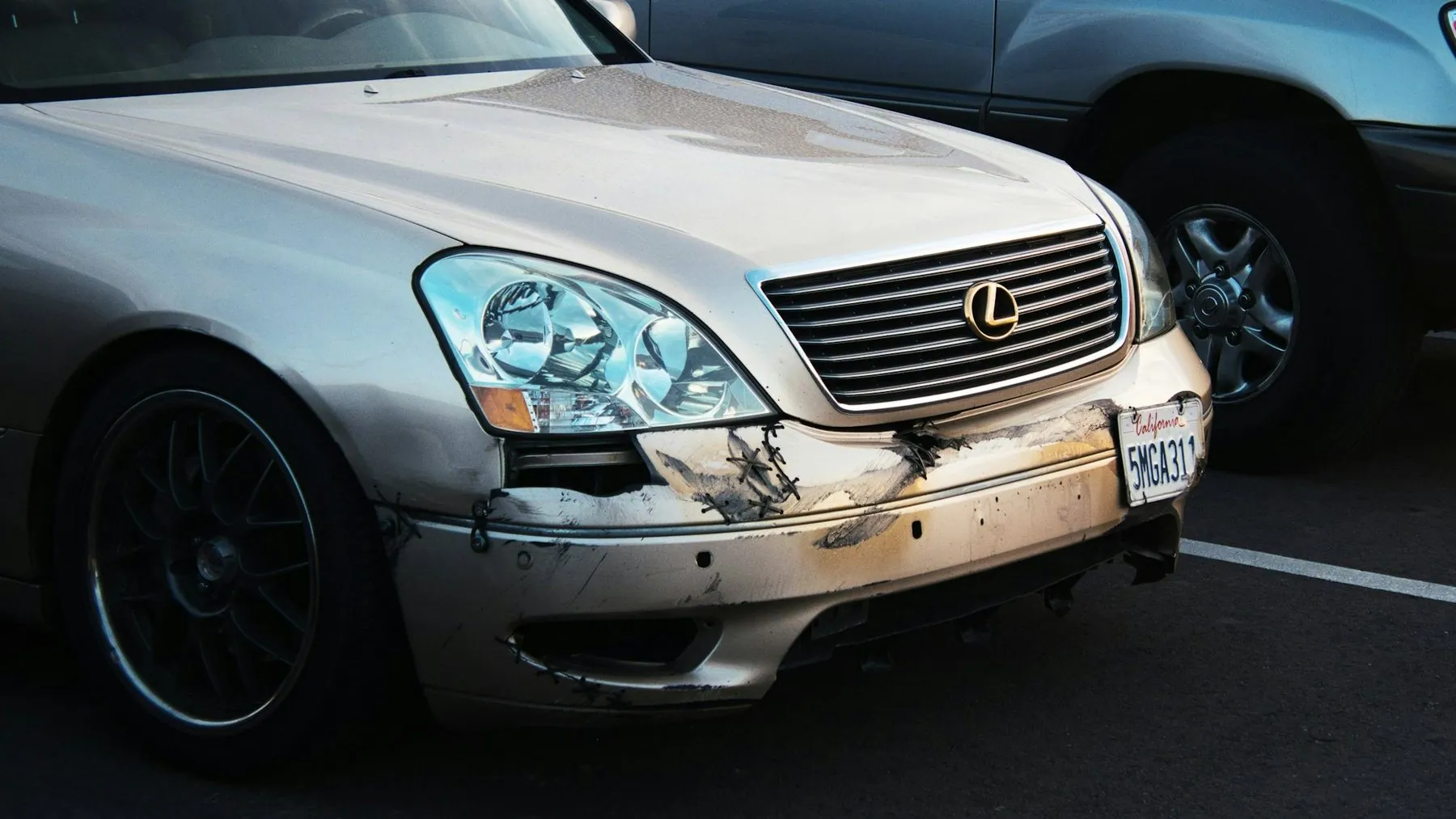A crumpled front wing and split bumper on a silver saloon parked nose-out between other cars