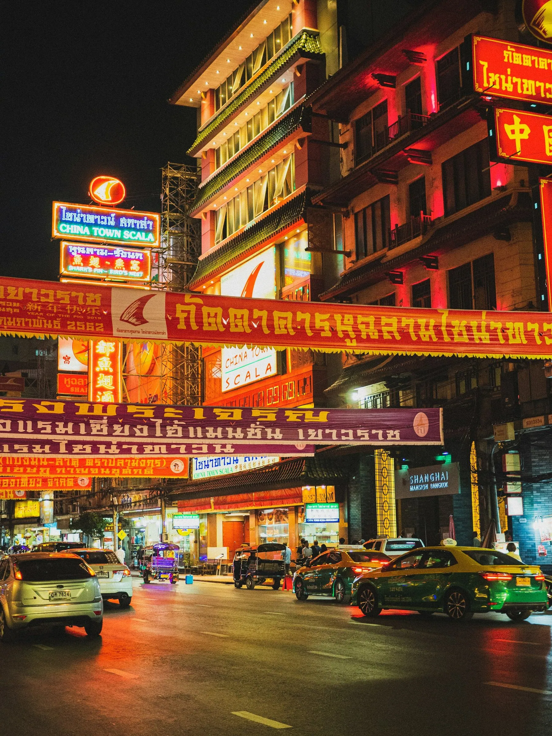 Cars and taxis at a standstill on a Thai street lit by neon shop signs at night