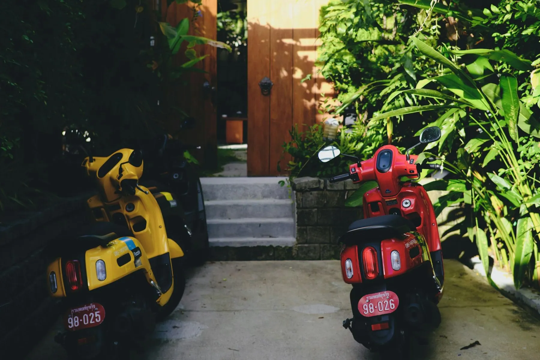 A yellow and a red scooter parked side by side on a kerb, Thai number plates facing the camera