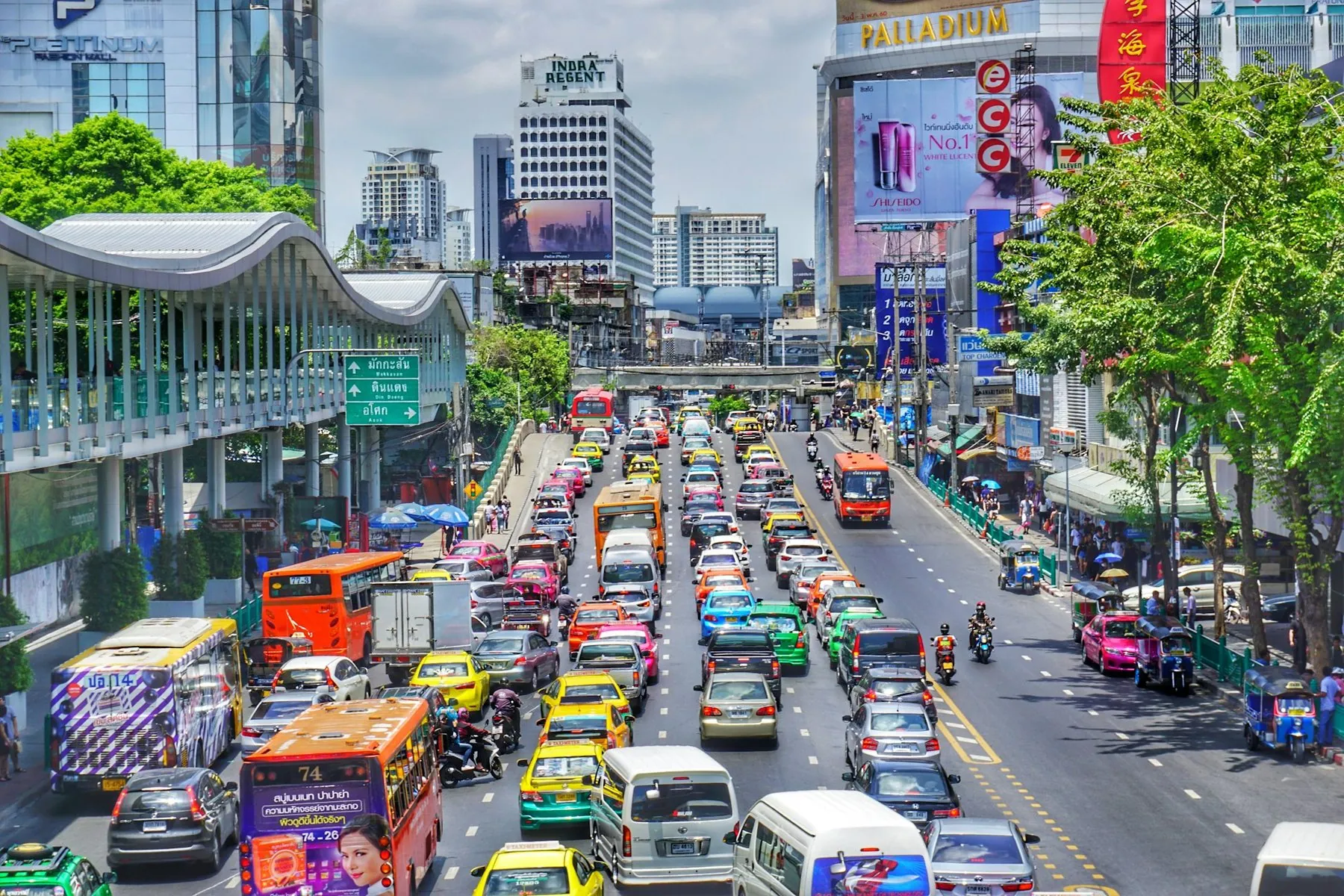Taxis, buses and private cars filling a wide Bangkok road under an elevated walkway