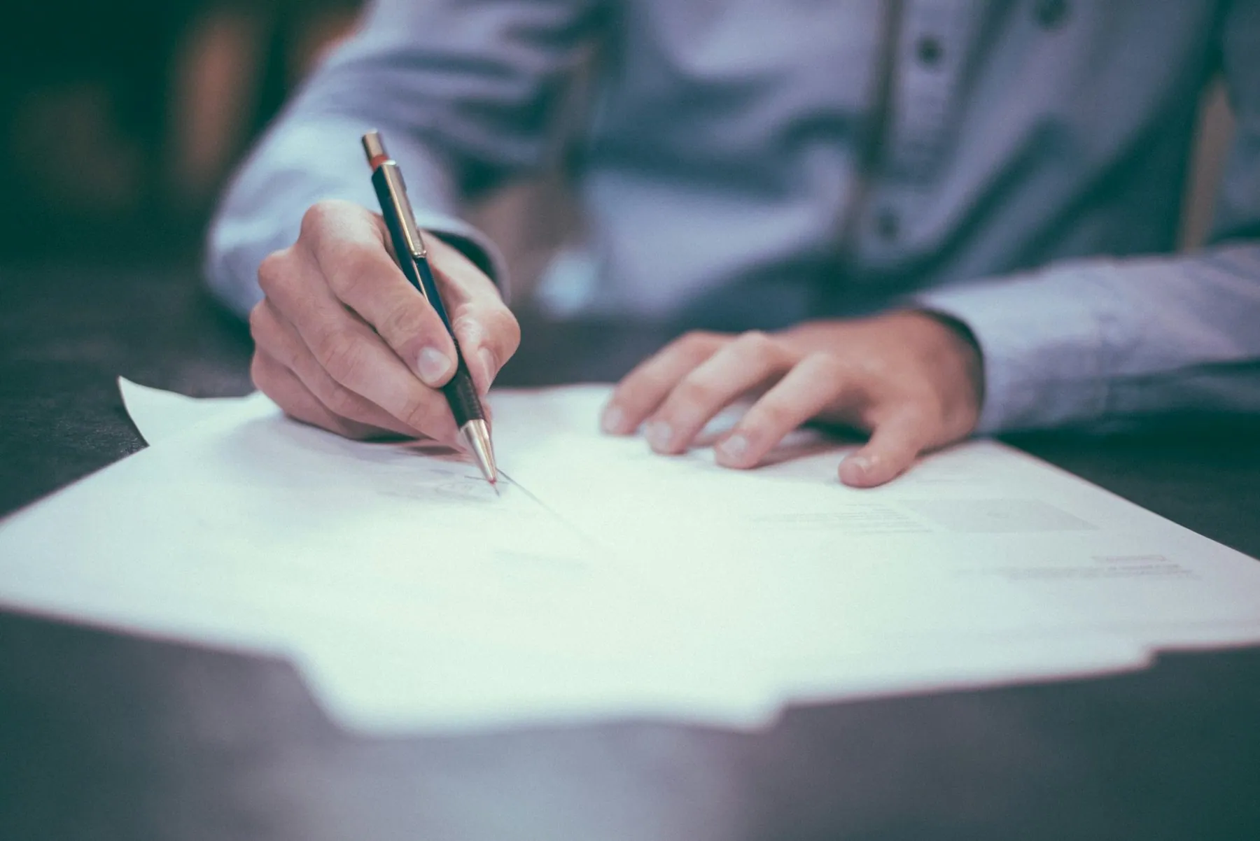 A hand writing on a sheaf of papers spread across a desk