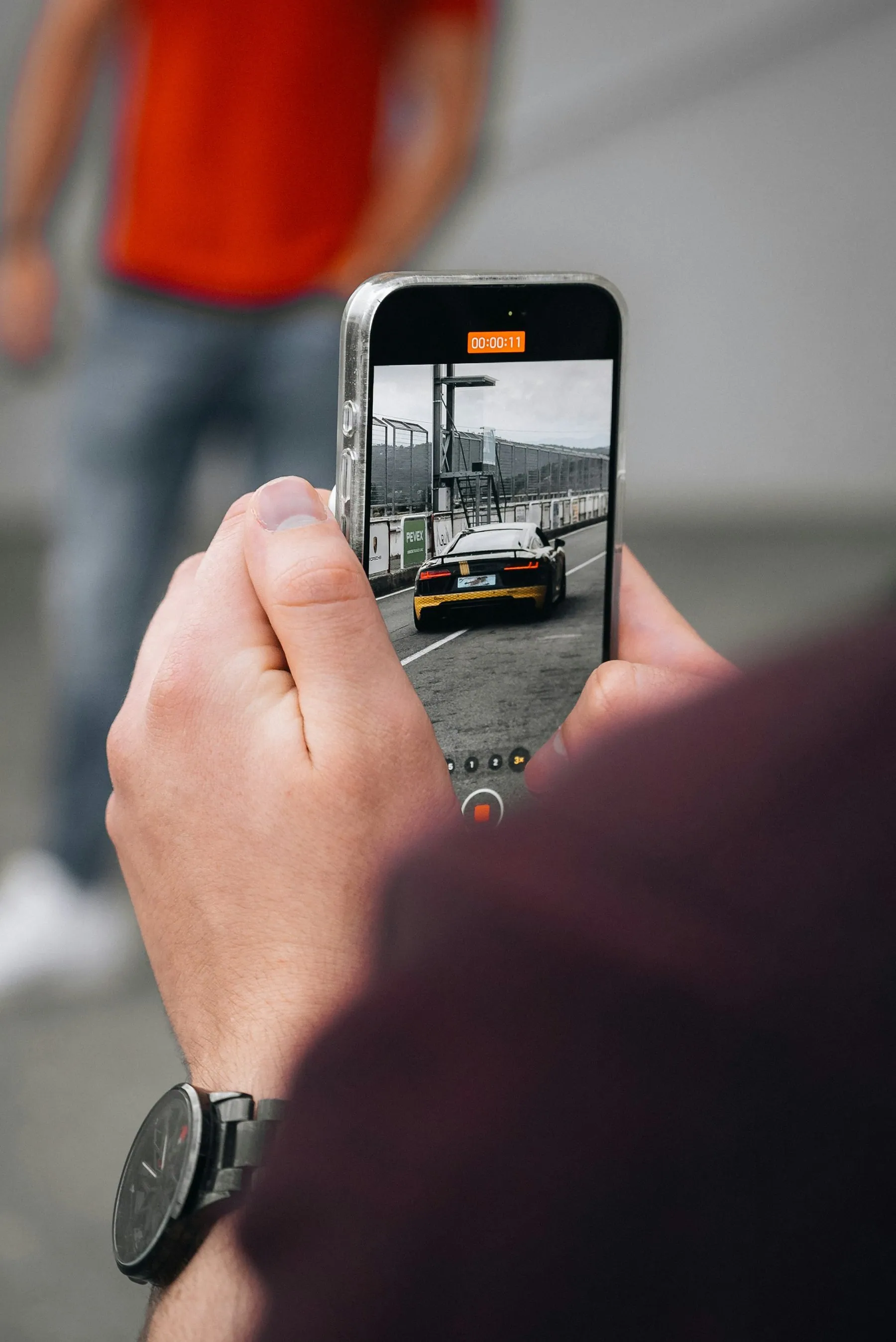 A person filming a vehicle on a phone held out in front of them
