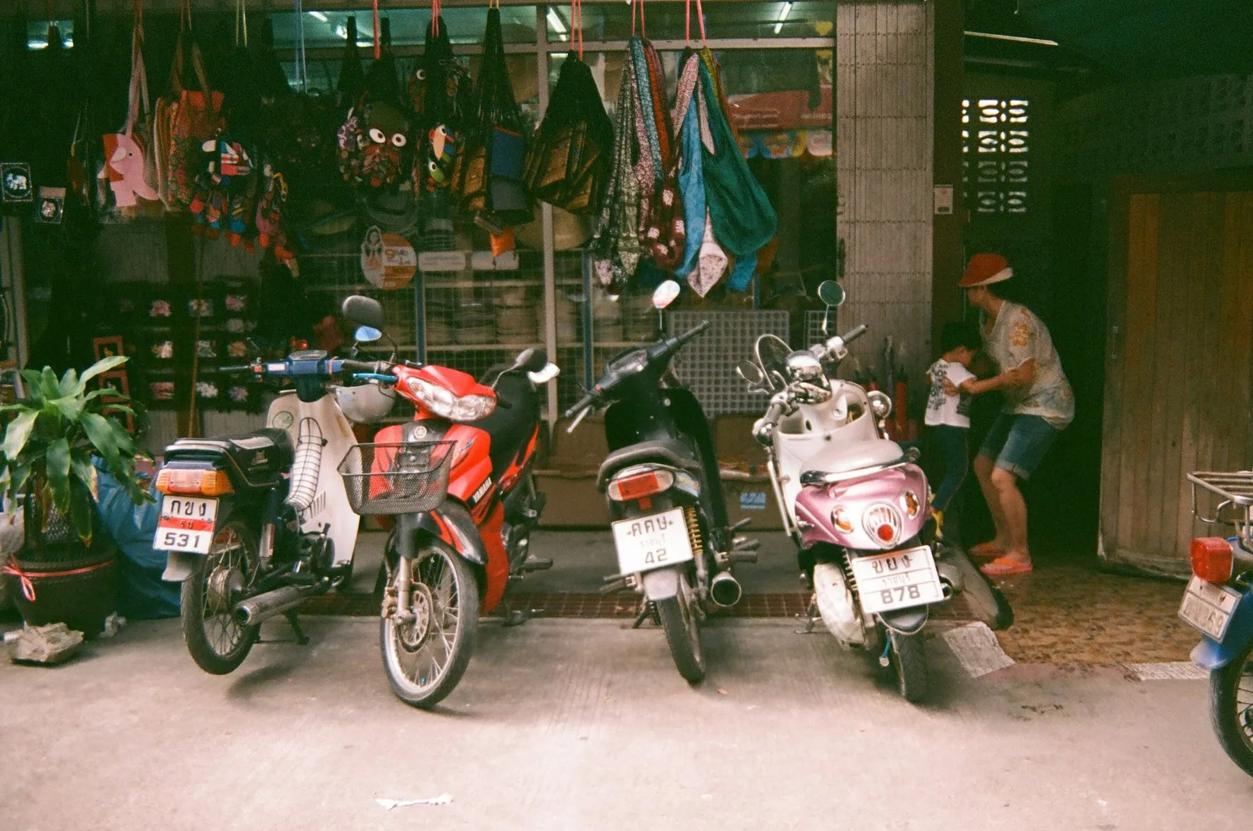 Scooters with Thai number plates parked on a pavement outside an open-fronted shop