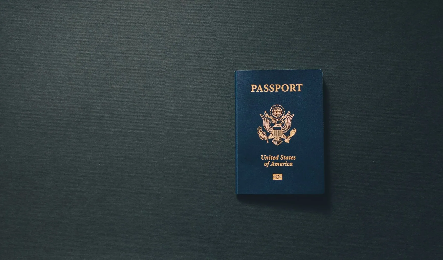A single passport lying closed on a dark grey surface