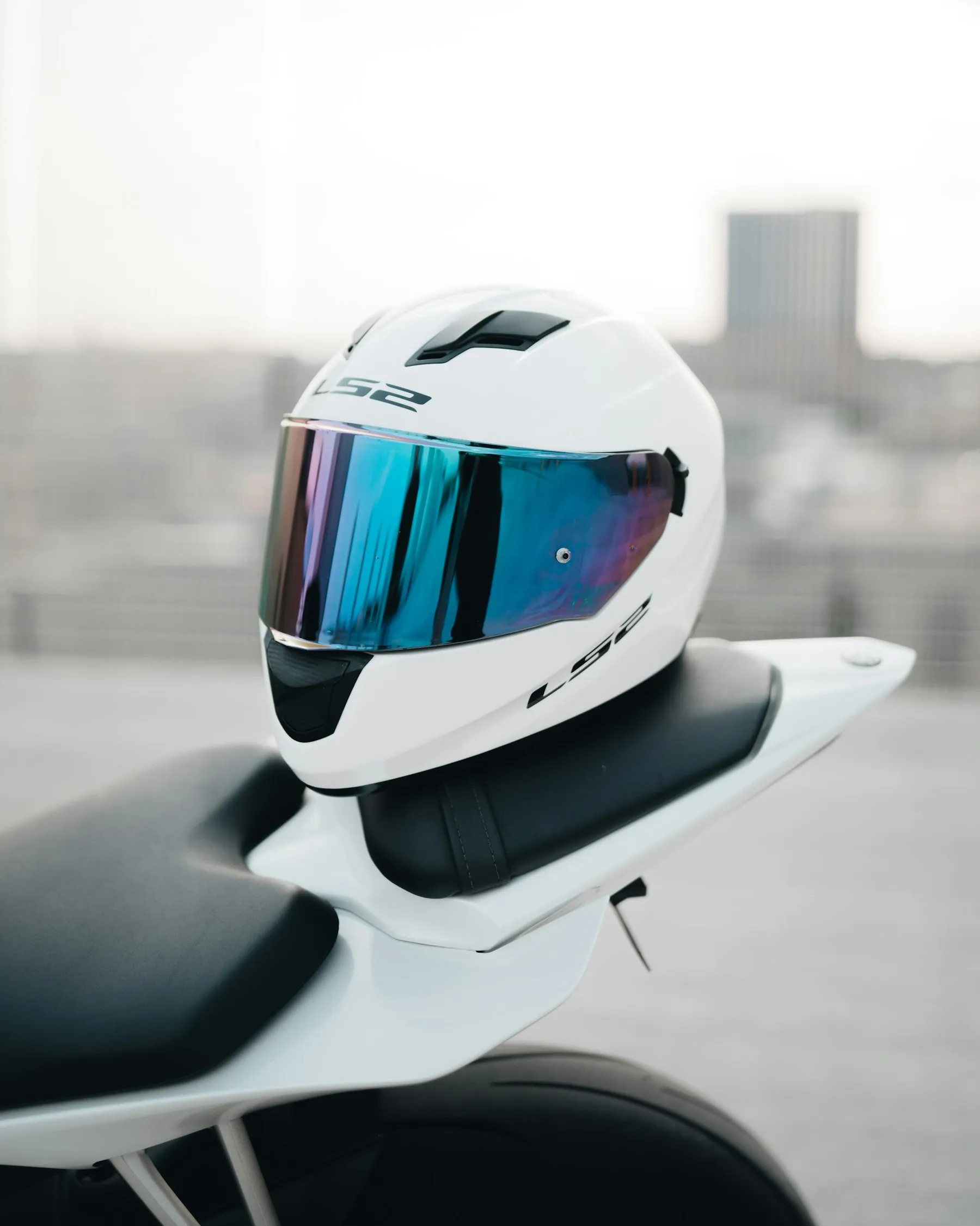 A white full-face helmet with a mirrored visor resting on a motorbike seat