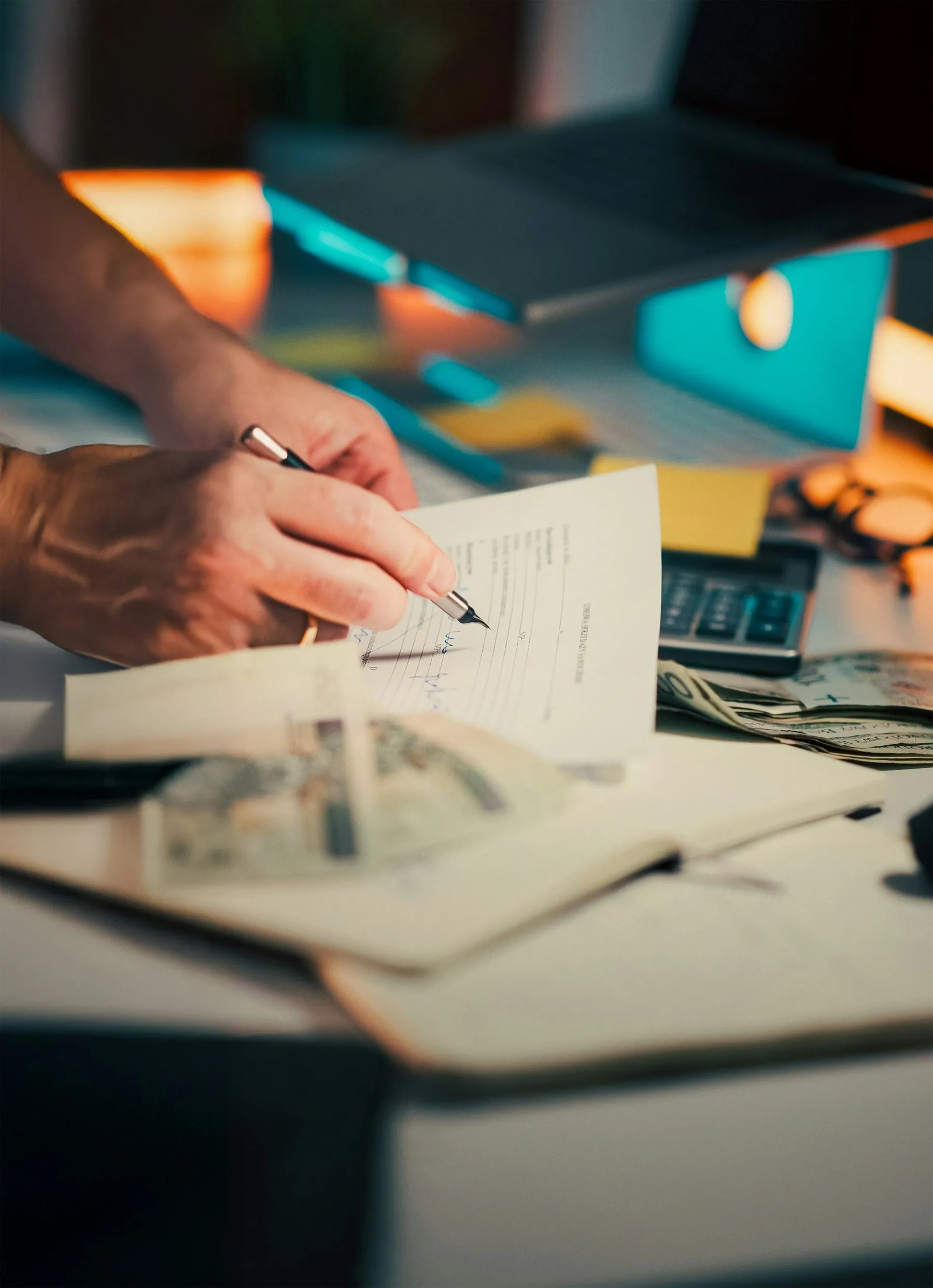 Hands signing a document across a desk with banknotes lying beside the paperwork