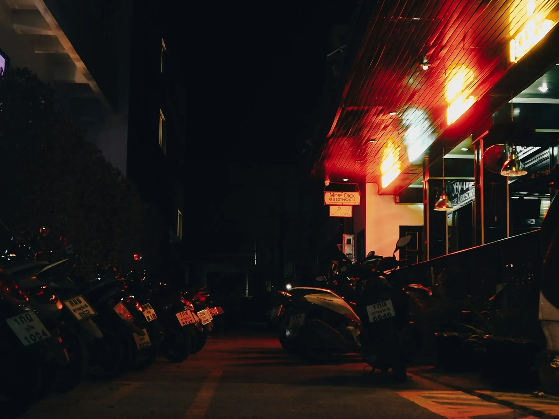 Scooters parked in a long line outside neon-lit bars on a Thai street after dark
