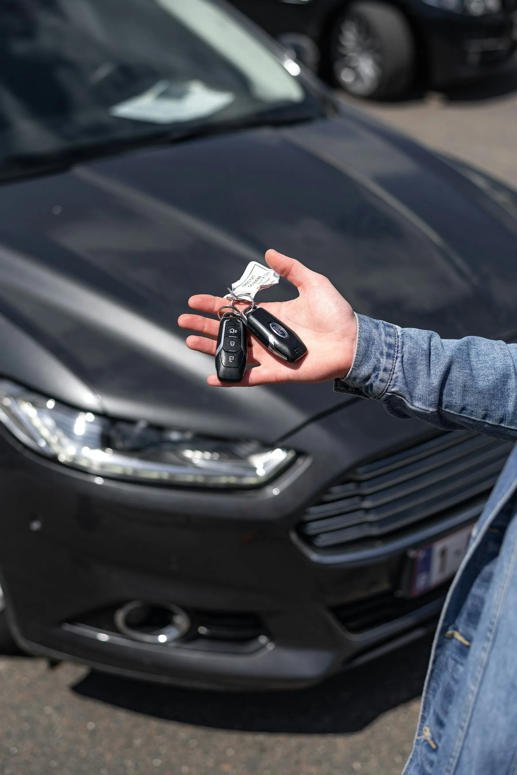 A hand holding a car key on its fob in front of a parked car