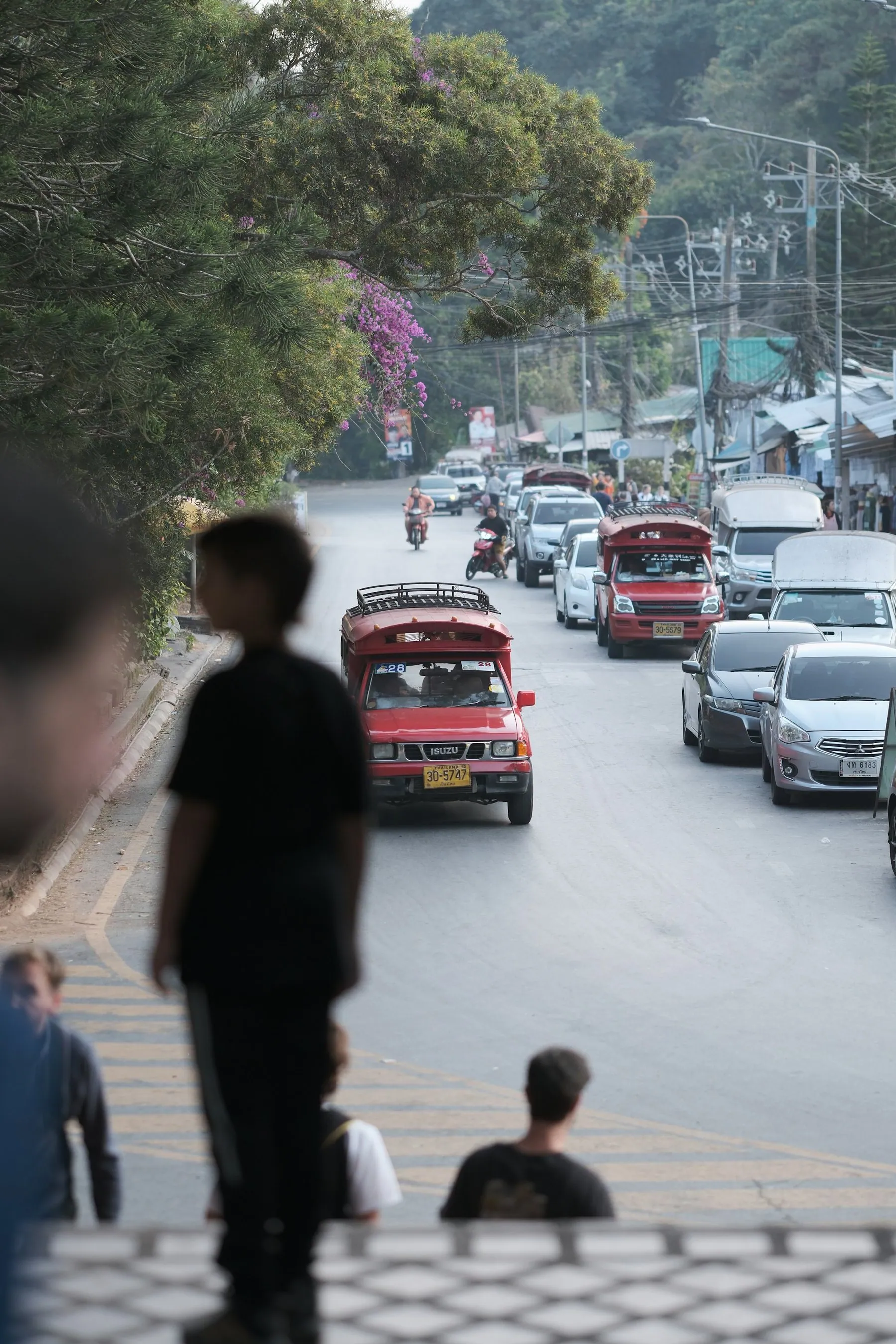 Red songthaews and cars climbing a busy hill road out of Chiang Mai