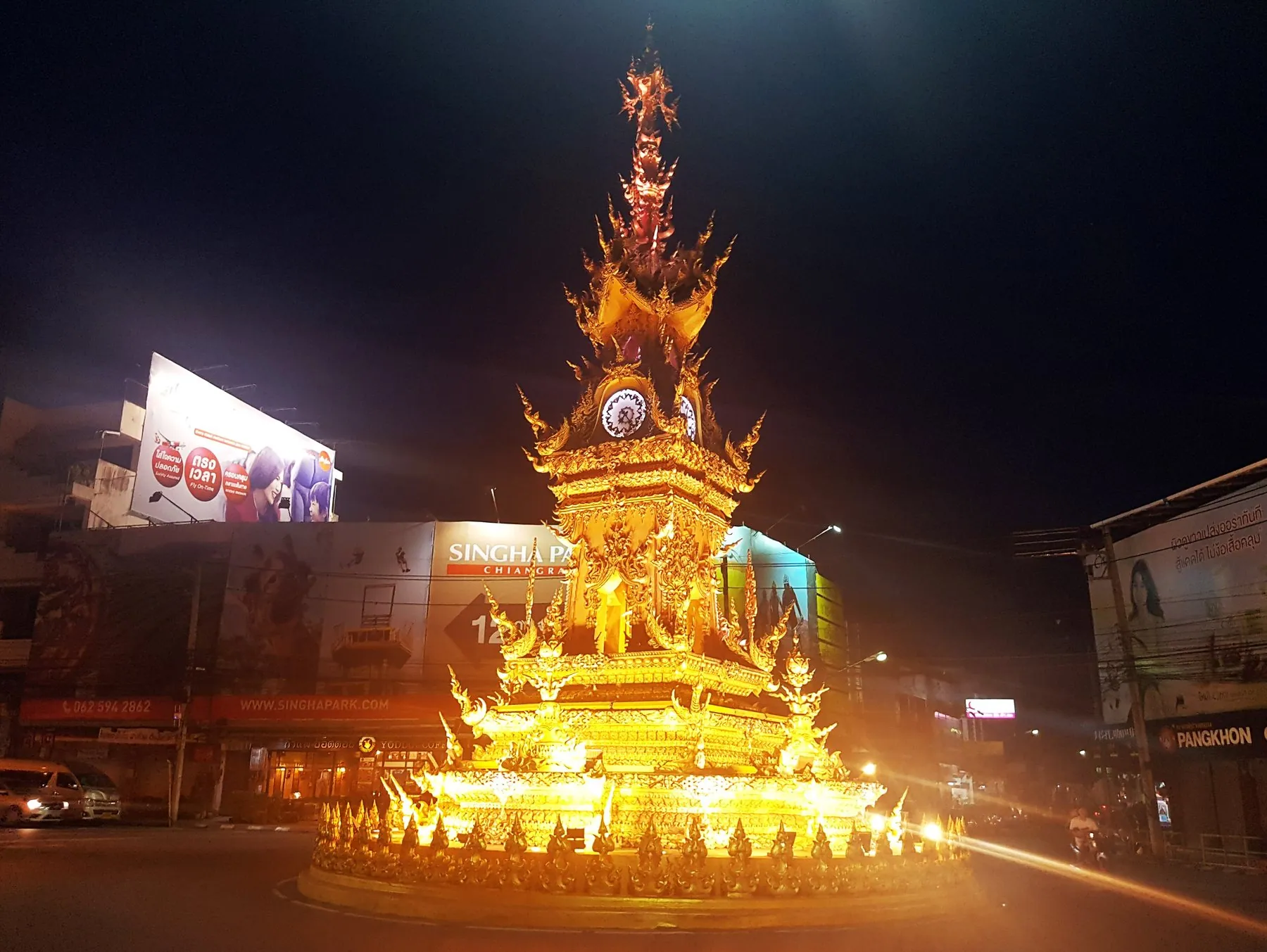 The golden clock tower on its roundabout in Chiang Rai, lit up with traffic circling at night
