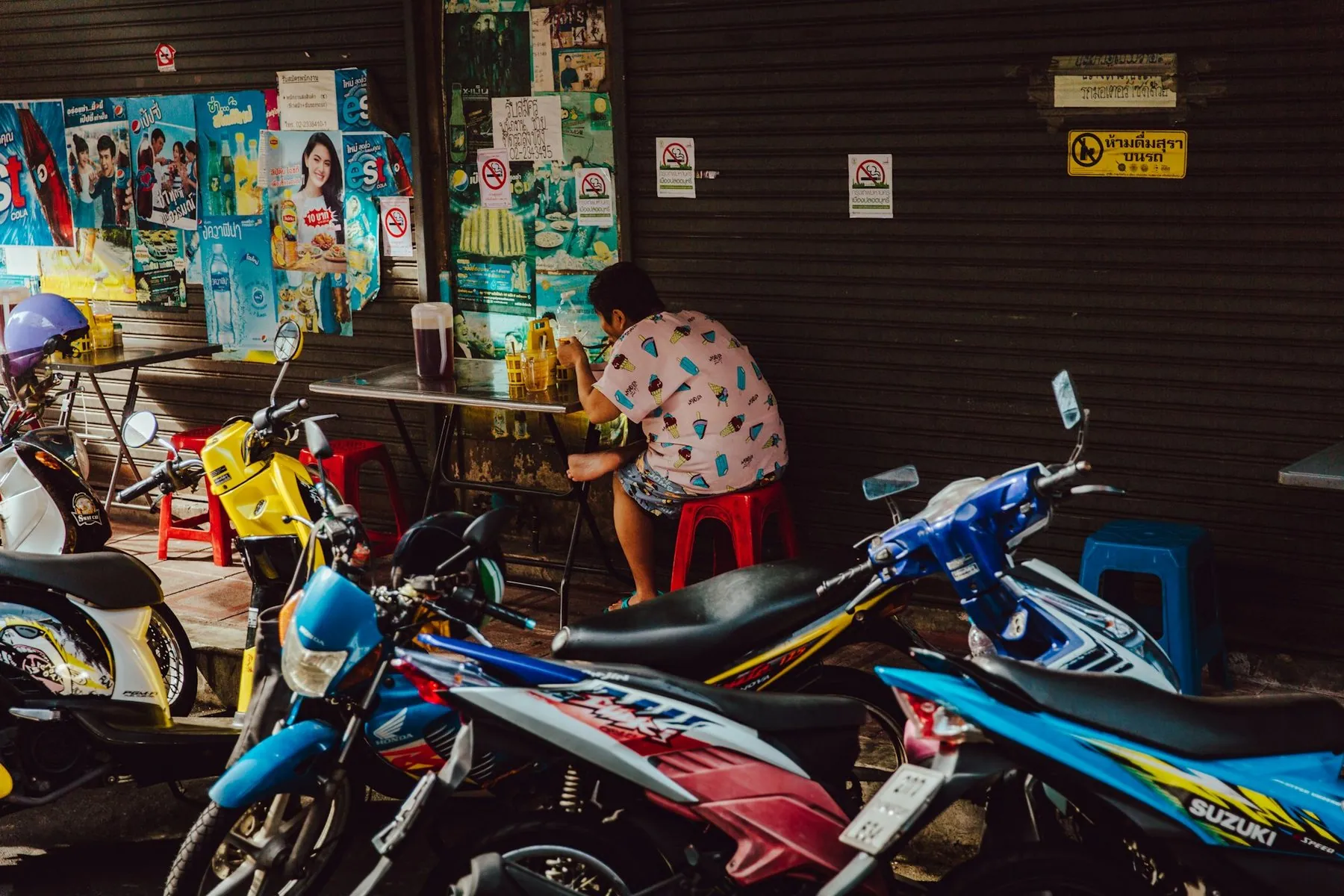 Blue and white step-through scooters lined up against a shop wall papered with Thai posters